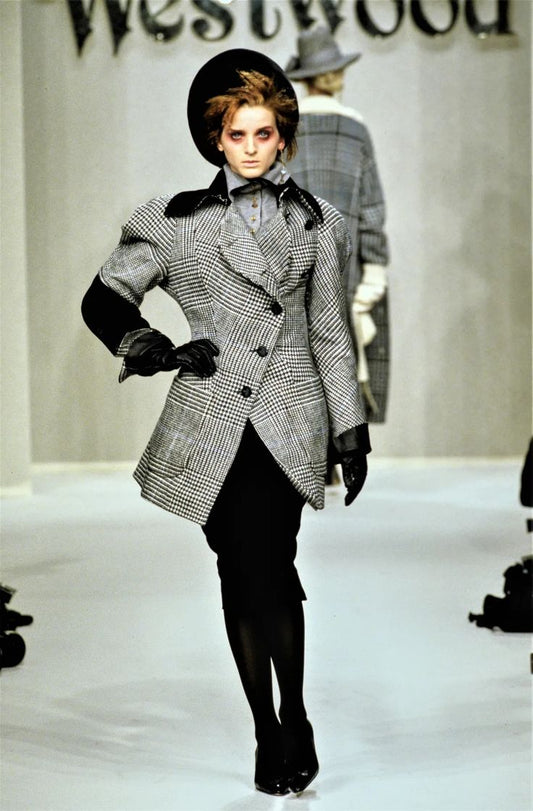 Model walking on a runway wearing a textured coat with a visible brand name in the background