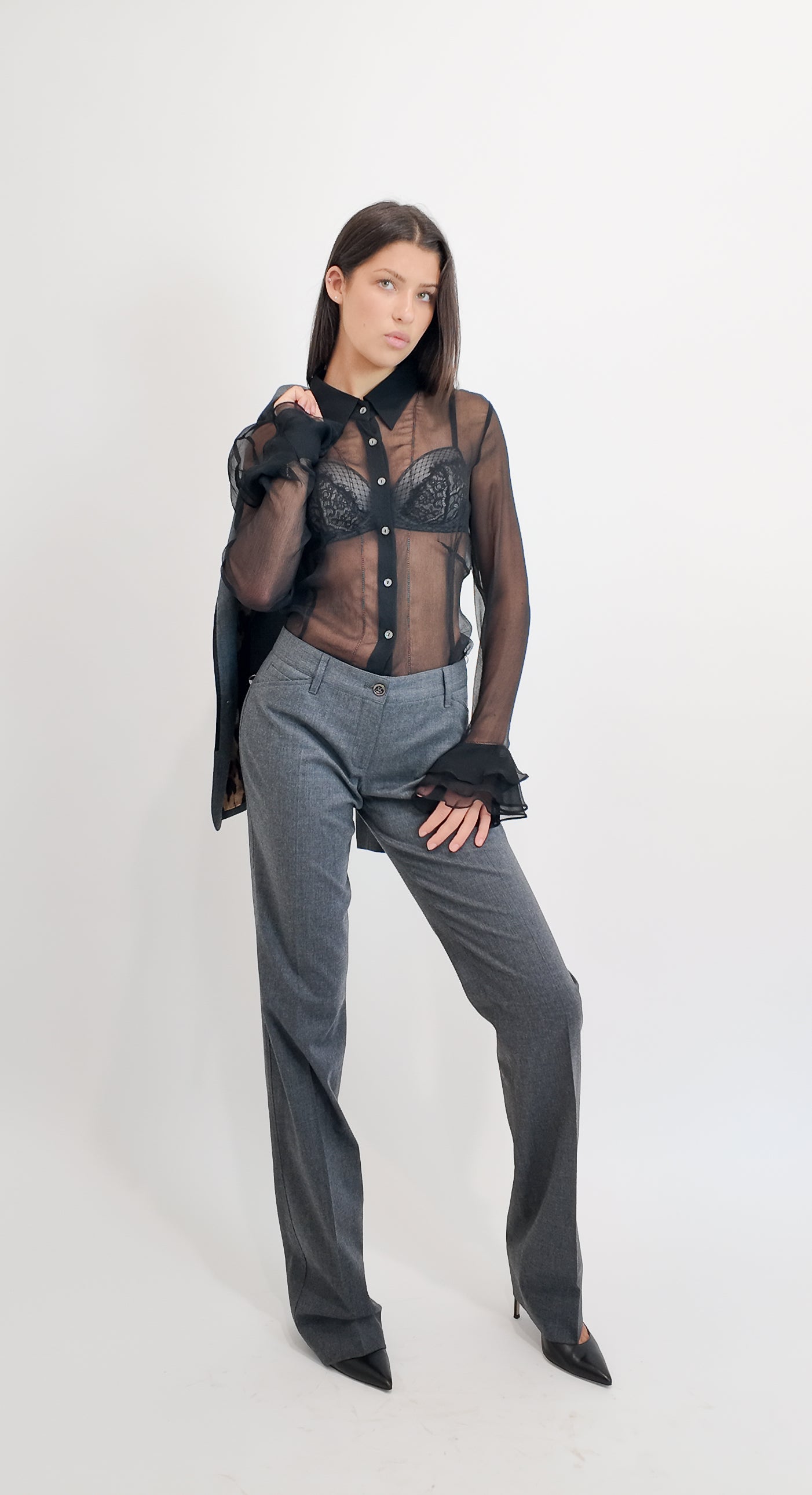 Woman wearing a black sheer top with buttons and gray pants on a white background