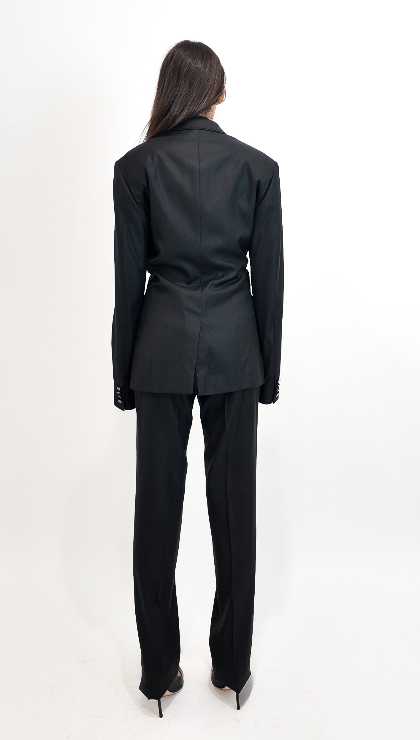 Person wearing a black suit standing against a white background