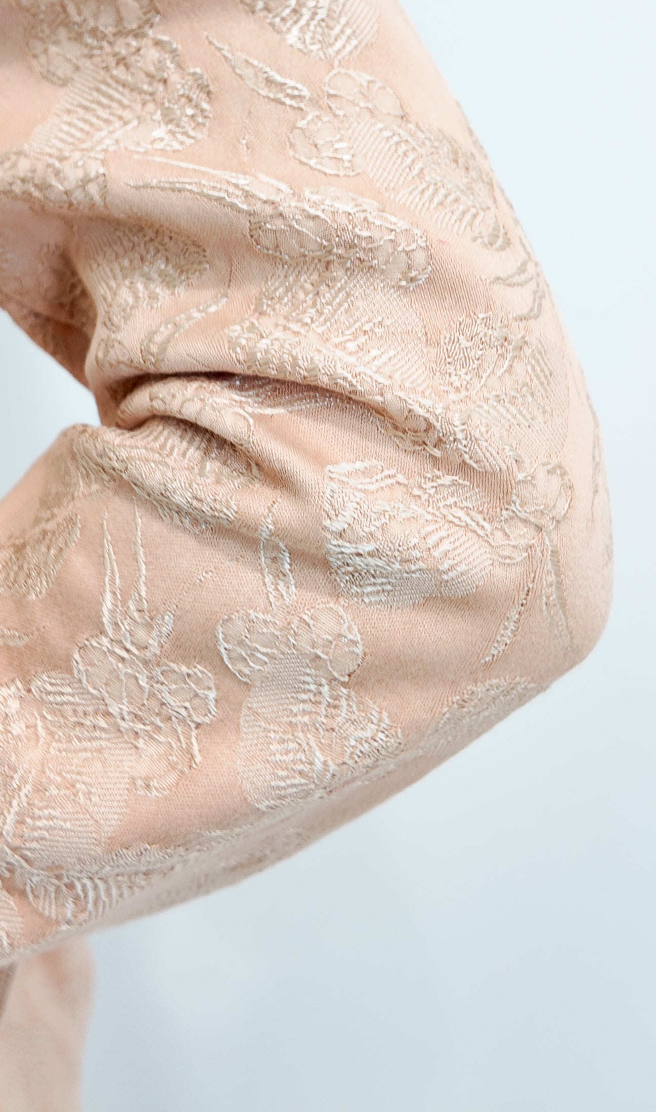 Close-up of a nude brocade garment on a white background