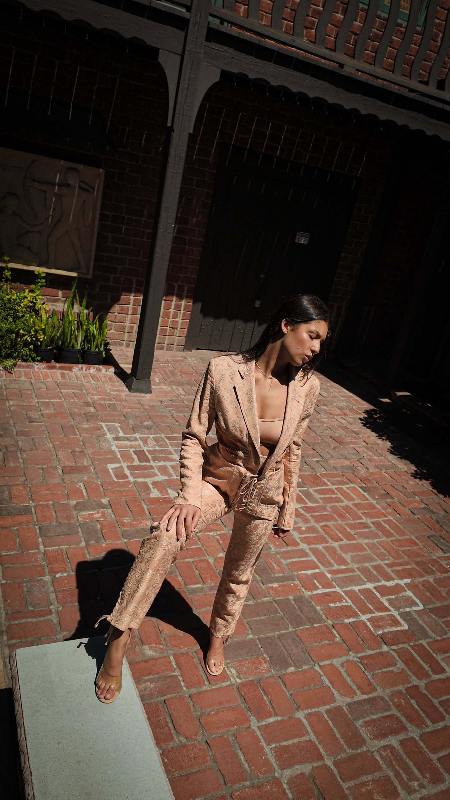 Woman in a nude suit standing on a brick path with a building in the background