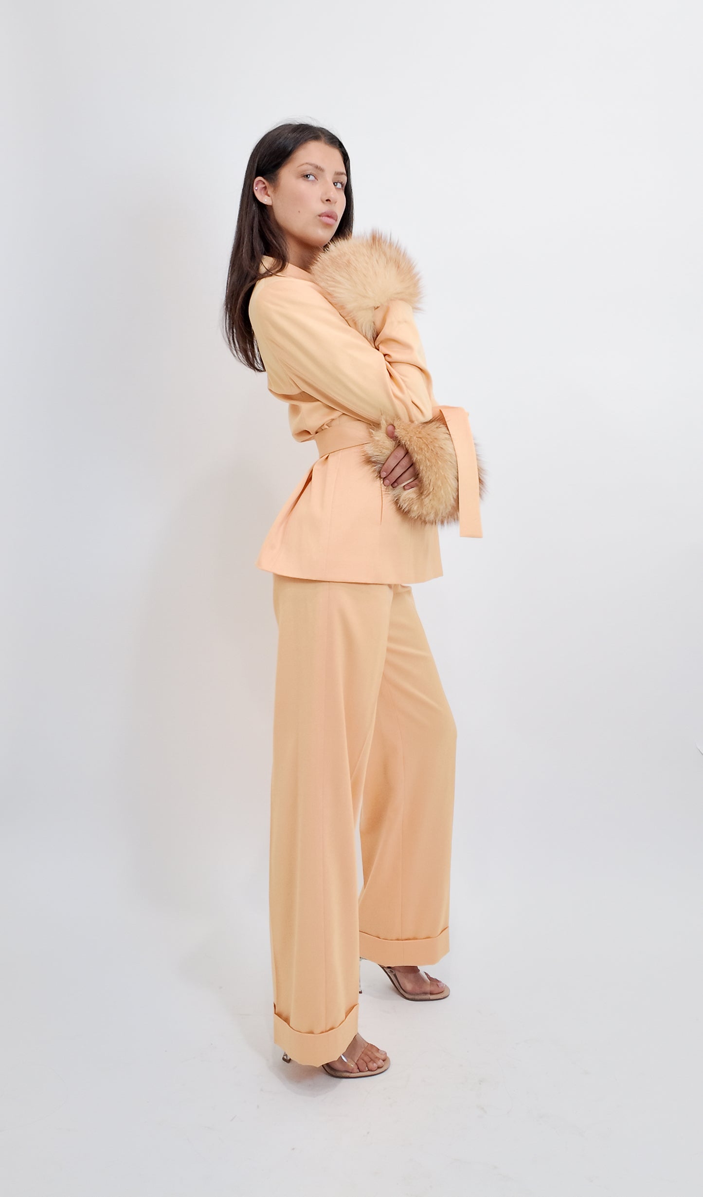 Woman wearing a peach suit with fur cuff against a white background
