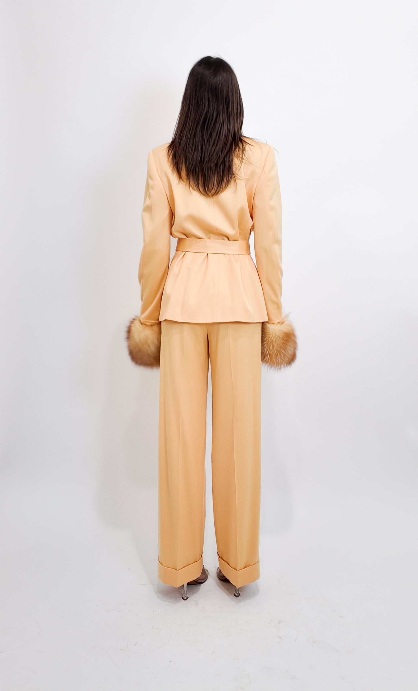 Woman wearing a peach suit with fur accents on a white background