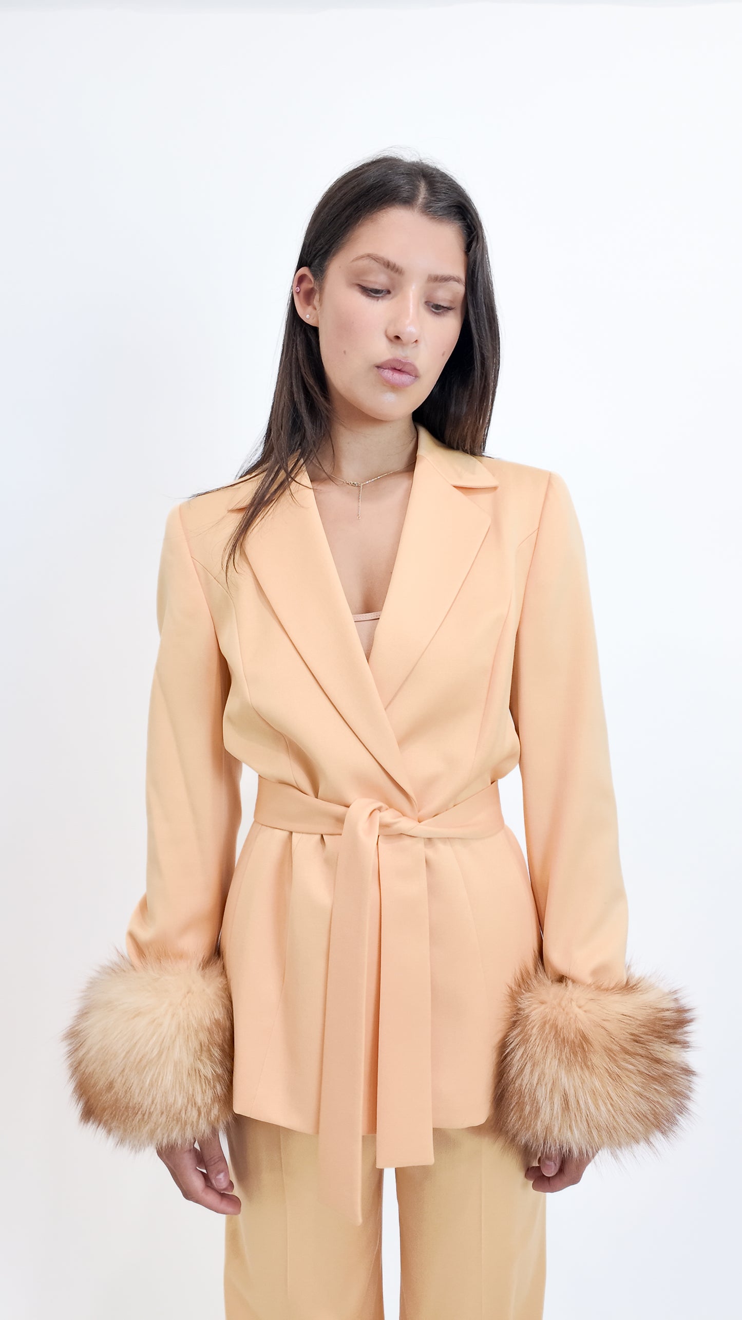 Woman wearing a peach-colored coat with fur cuffs on a white background