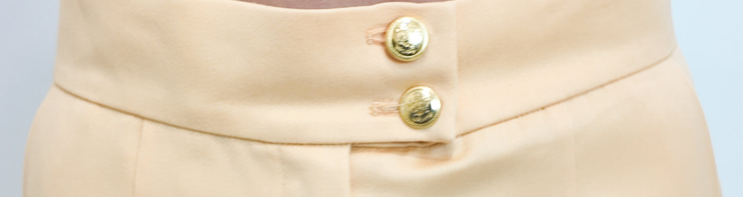 Close-up of peach pants with gold buttons on a light gray background