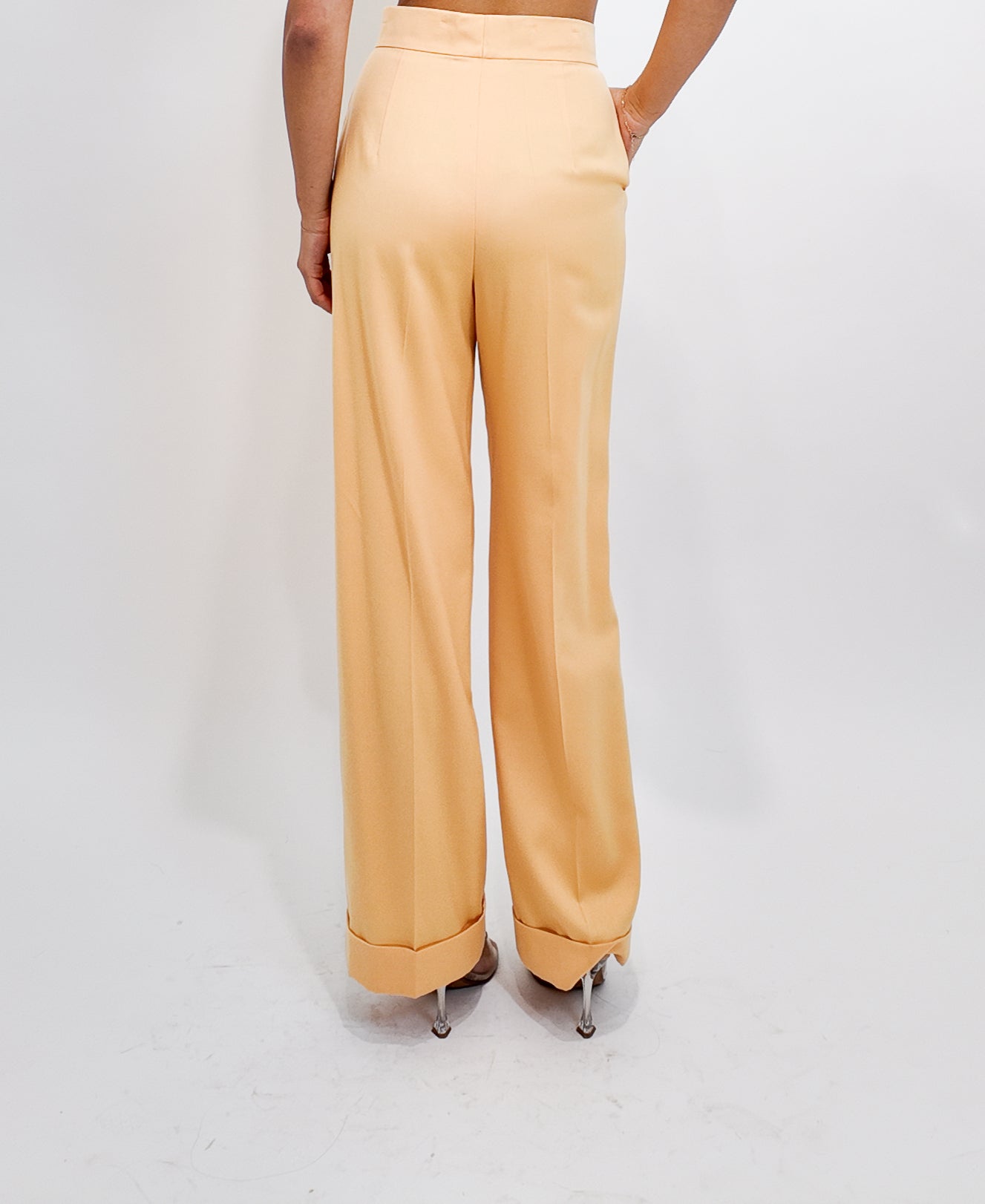 Person wearing peach high-waisted pants on a white background