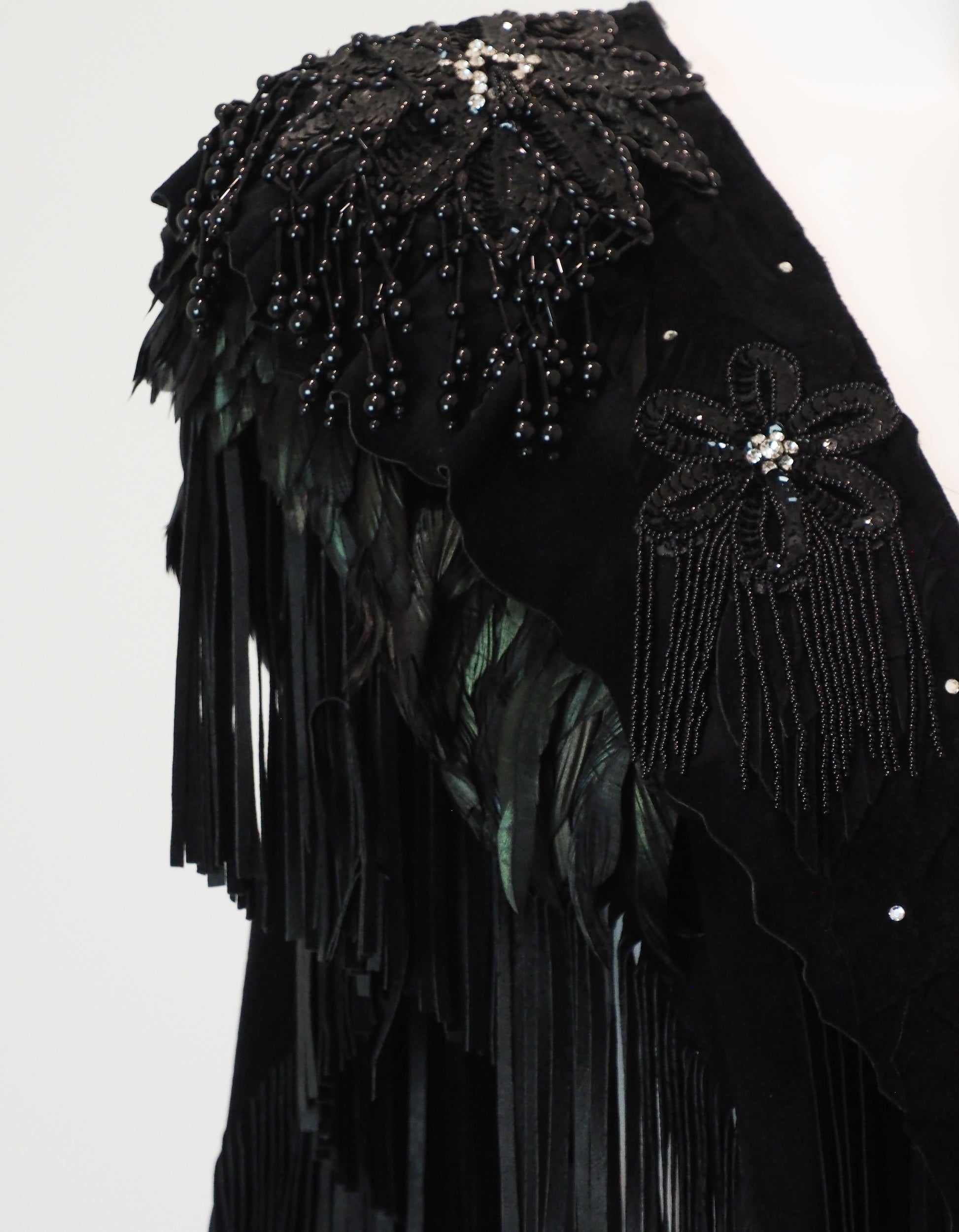 Black garment shoulder with floral embellishments and fringe details on a white background