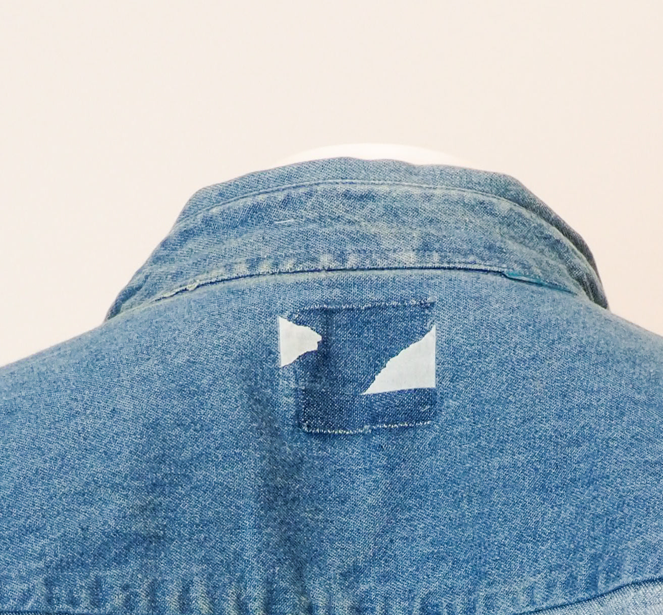 Close-up of a blue denim jacket with a brand logo on a beige background