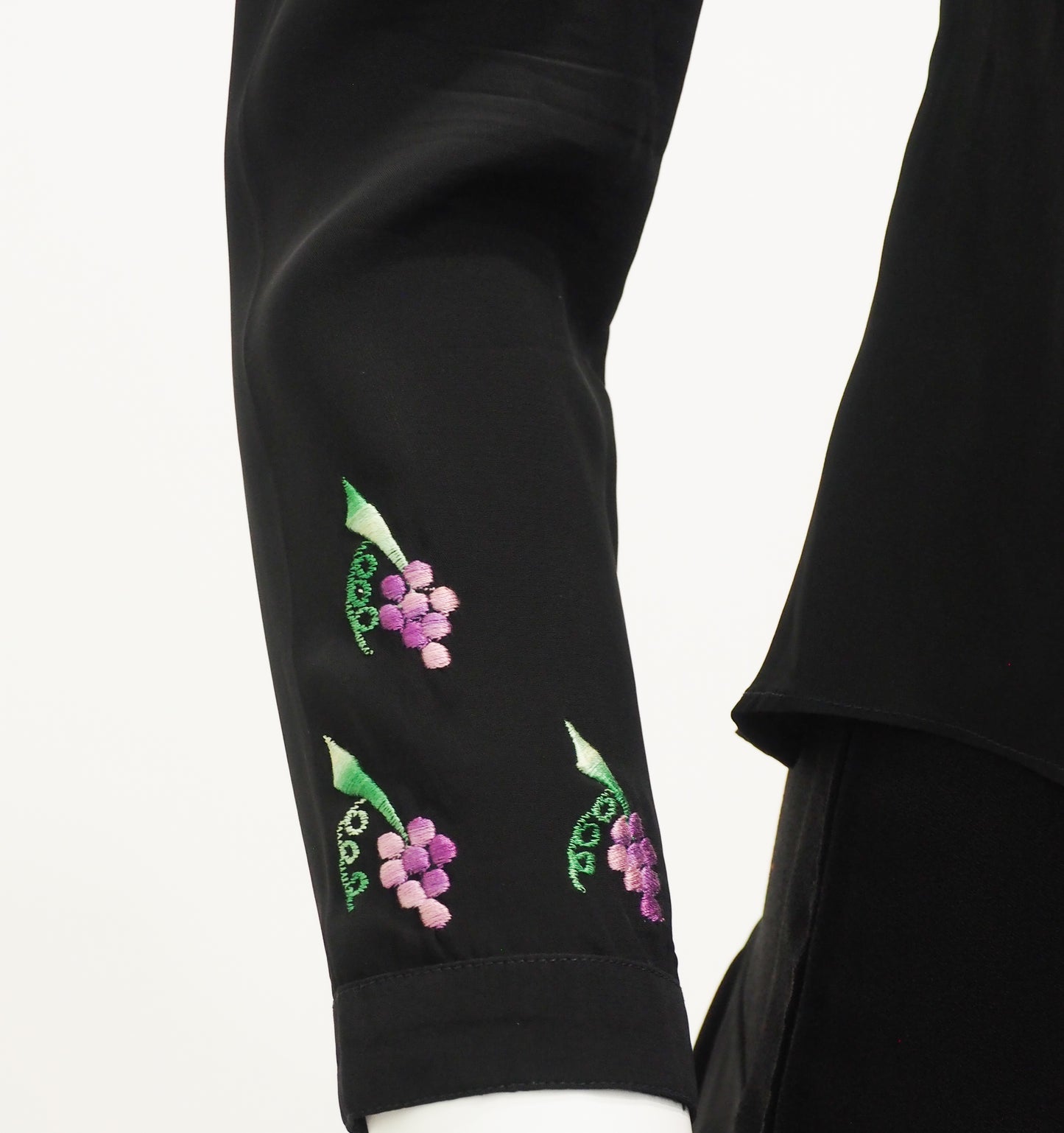 Black garment with embroidered green leaves and pink flowers on a white background