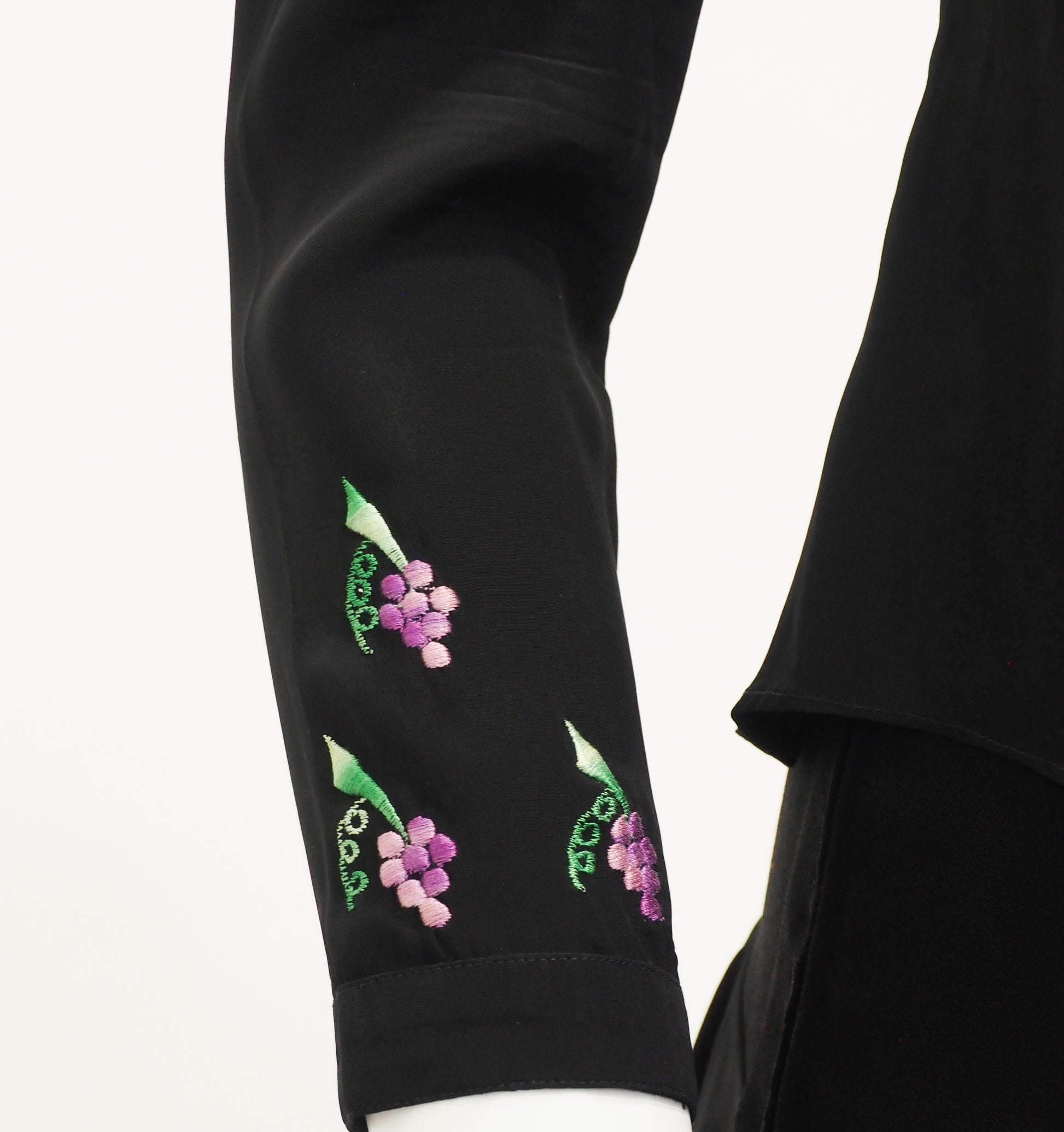 Black garment with embroidered green leaves and pink flowers on a white background