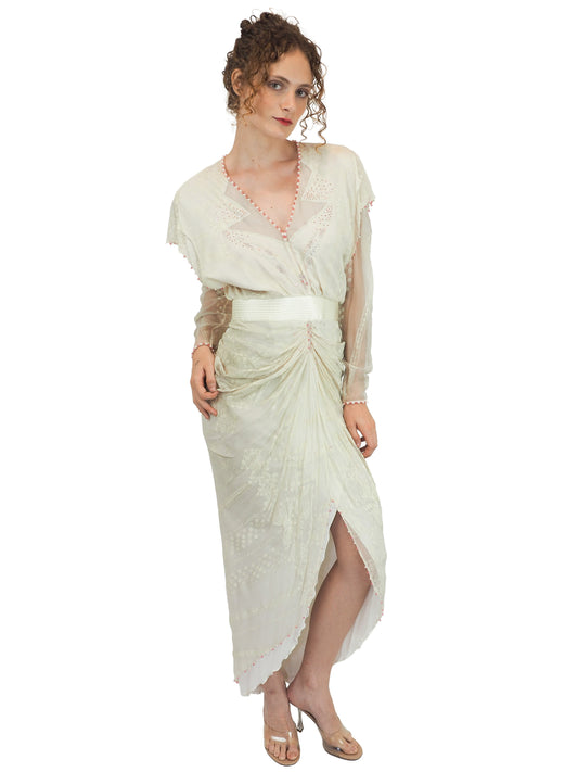 A vintage Zandra Rhodes cream-colored bridal wedding dress with sheer long sleeves, pink beaded detailing, a gathered waist, and a draped skirt