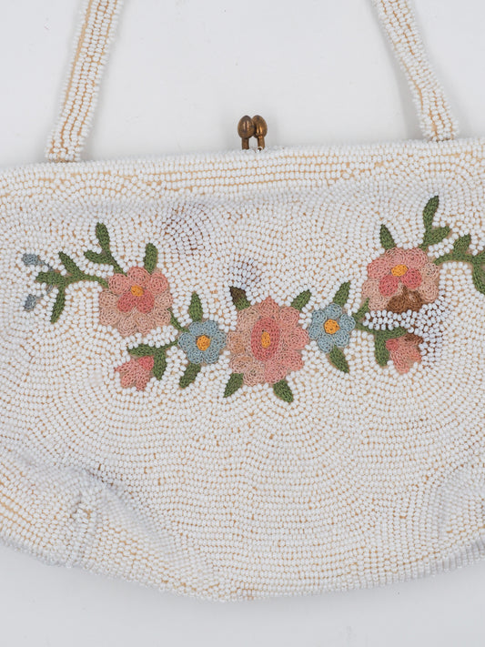 A vintage beaded handbag in a warm off-white/cream tone, featuring a floral embroidered pattern with pink, orange, and green details across the front, a small gold-tone clasp, and shoulder straps.
