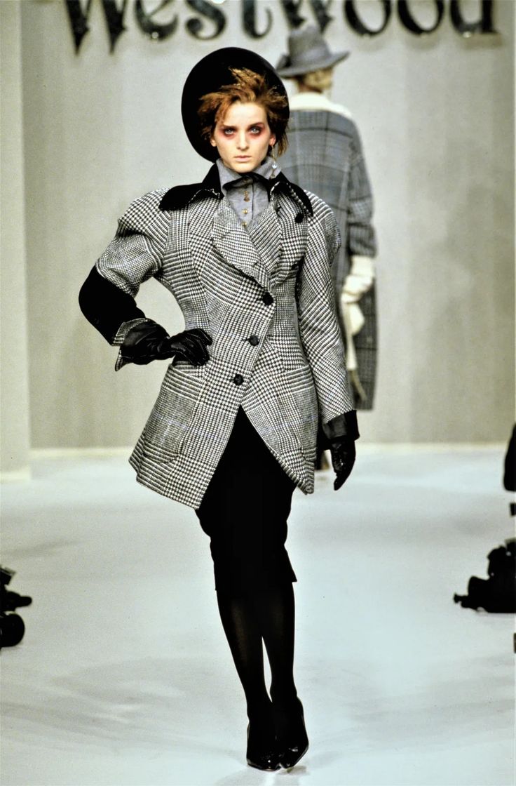 Model walking on a runway wearing a textured coat with a visible brand name in the background