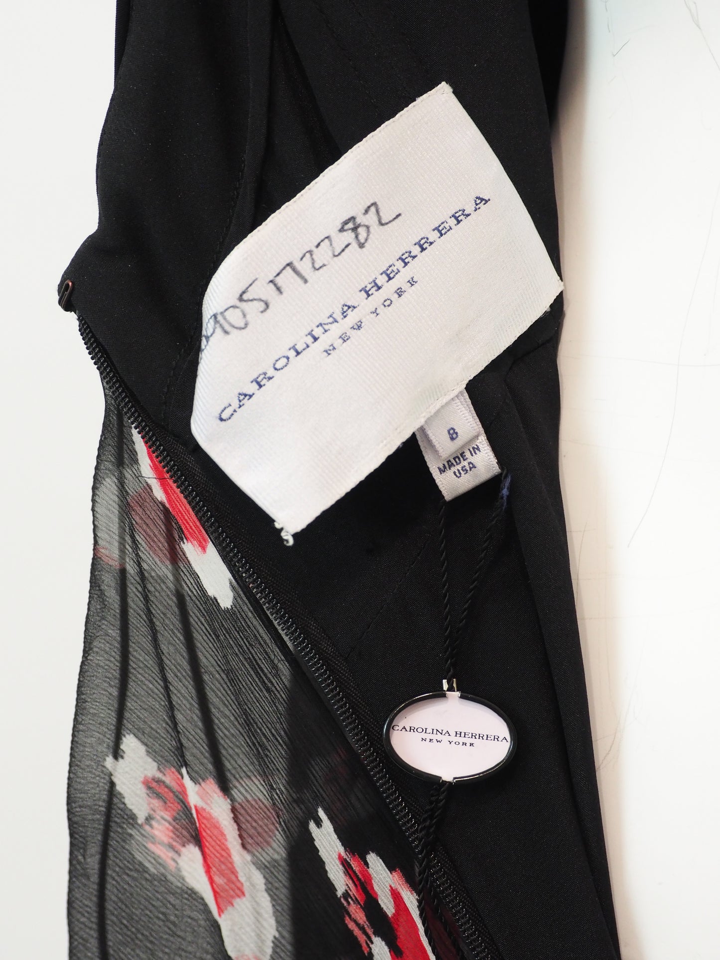 Close-up of a Carolina Herrera garment showing a white brand label, a black zipper, sheer black mesh, and a red, white, and black floral patterned fabric.