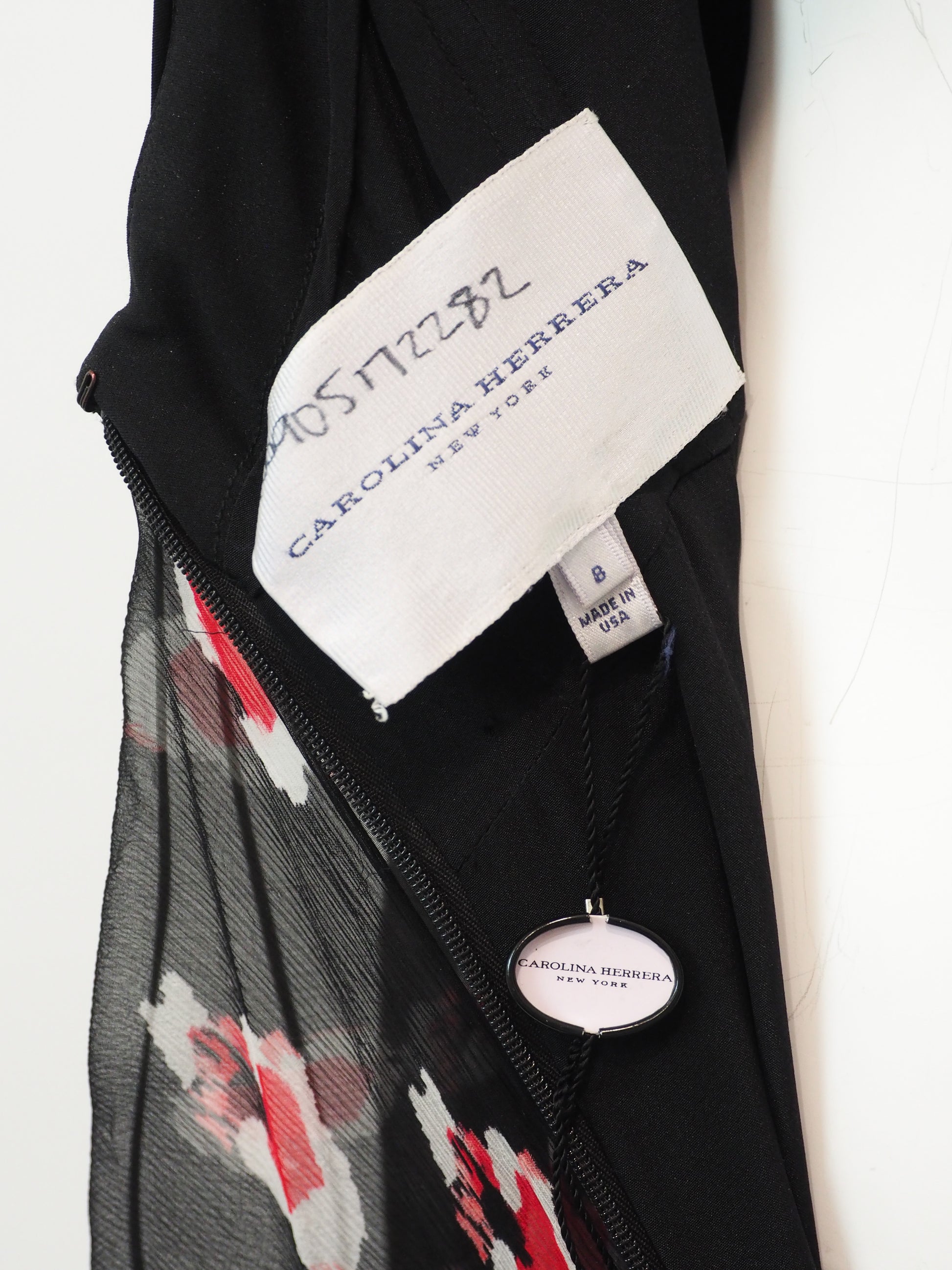 Close-up of a Carolina Herrera garment showing a white brand label, a black zipper, sheer black mesh, and a red, white, and black floral patterned fabric.