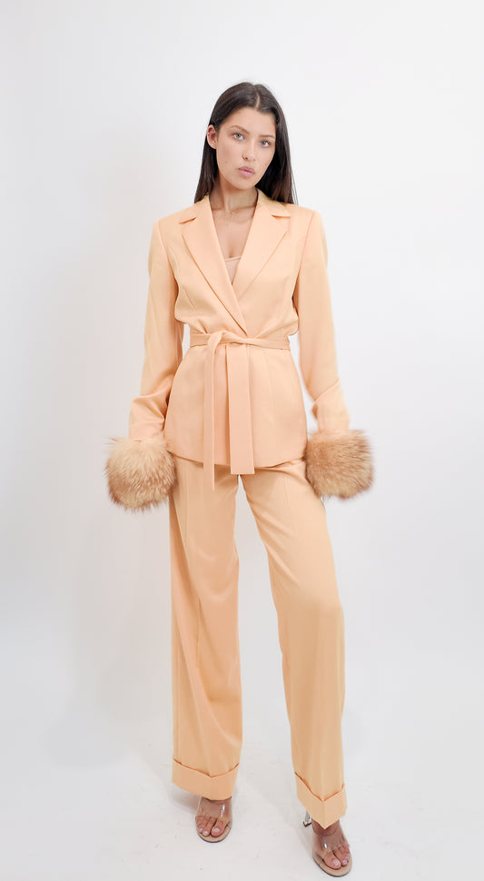 Woman wearing a peach suit with fur cuffs on a white background