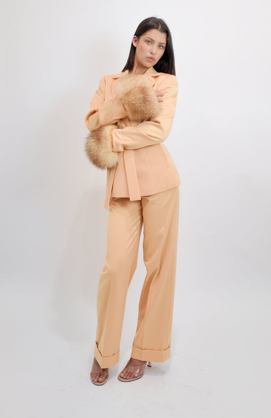 Woman wearing a peach suit with fur accents on a white background