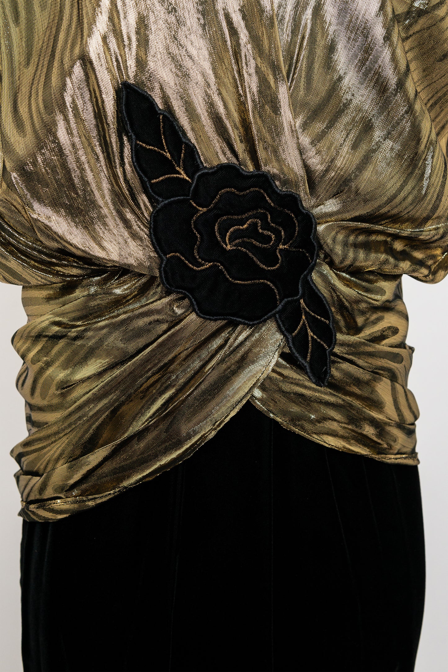 Gold velvet top with black floral accessory on a white background