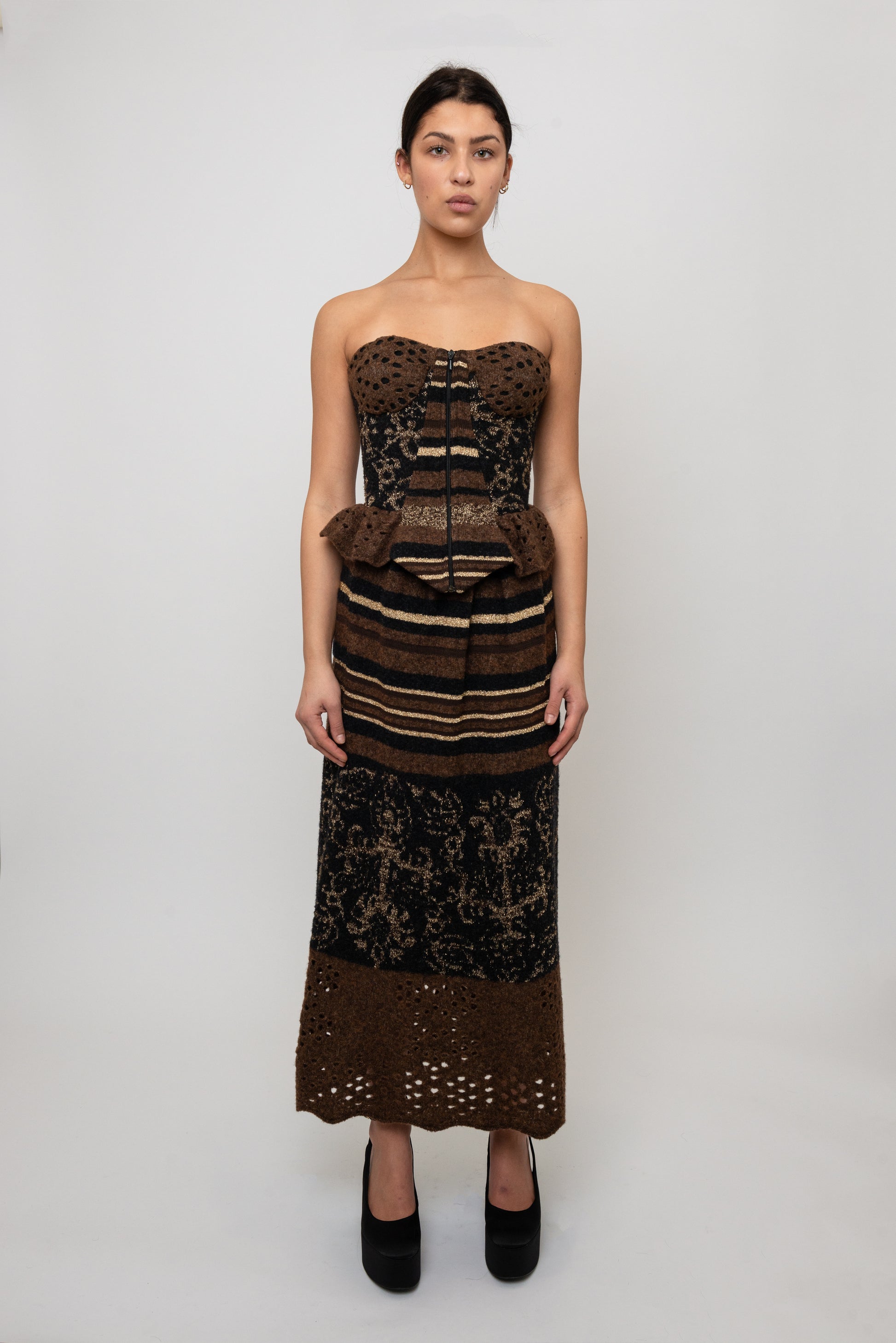 Woman wearing a strapless knit top with intricate patterns and a matching skirt on a white background