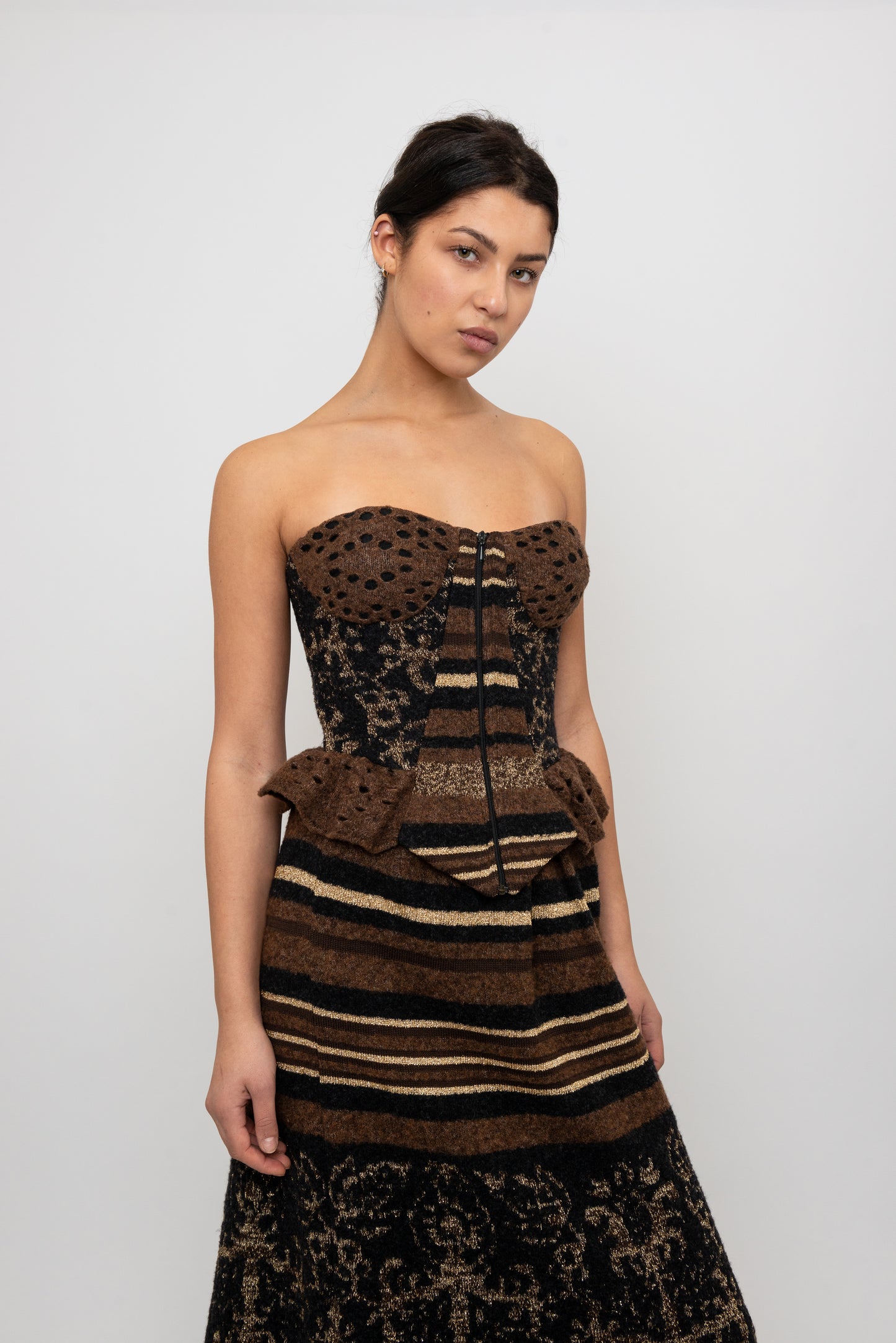 Woman wearing a strapless, peplum knit top  with a textured pattern skirt on a white background