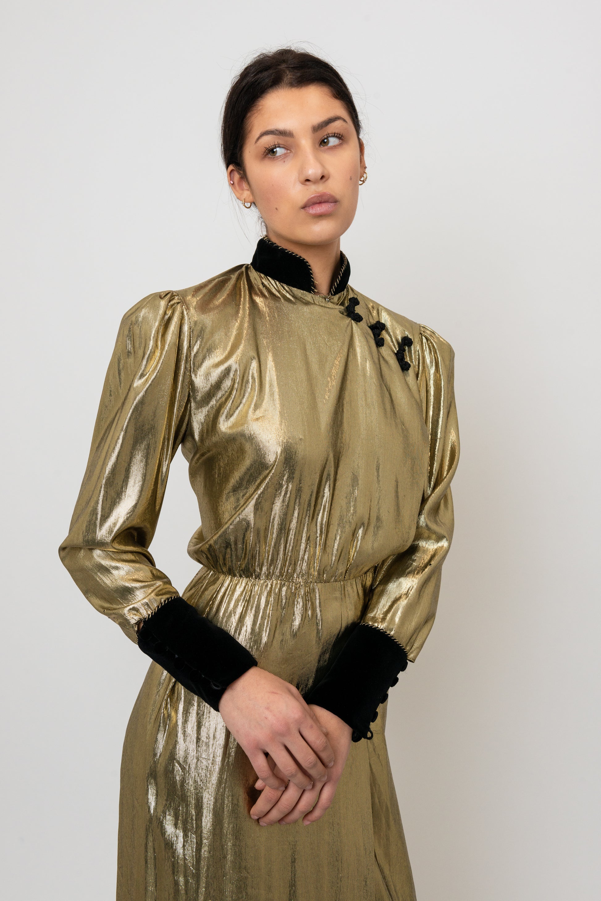 Woman wearing a gold metallic dress with black cuffs against a white background