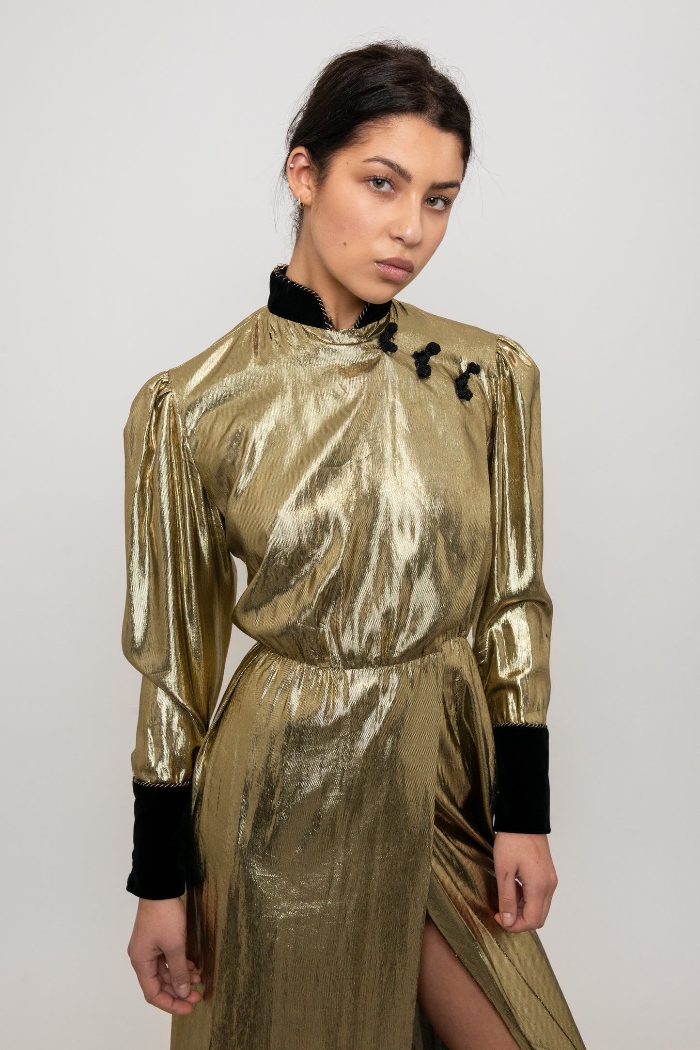 Woman wearing a gold metallic dress with black accents on a white background
