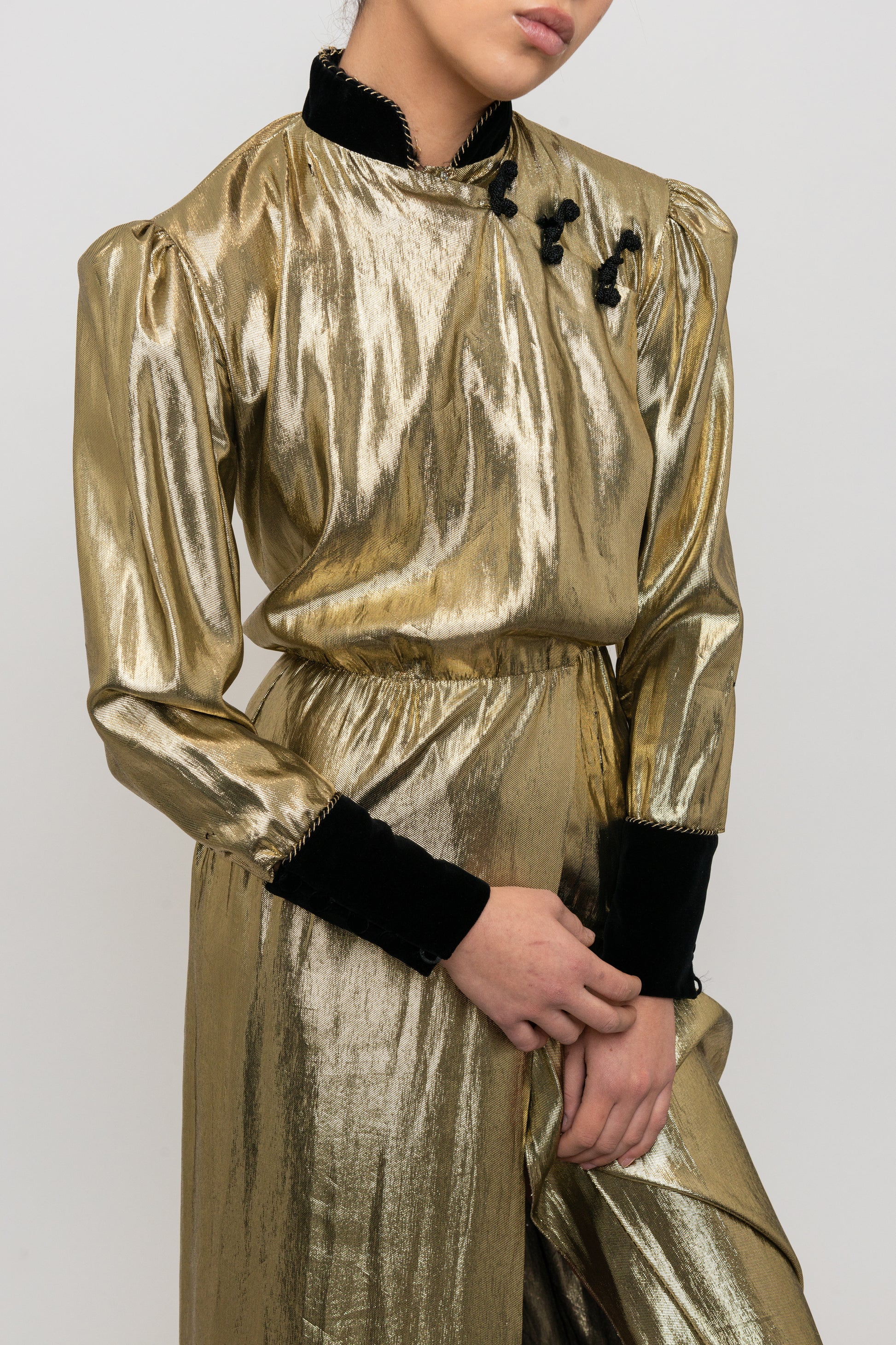 Gold metallic outfit with black cuffs and collar on a plain background