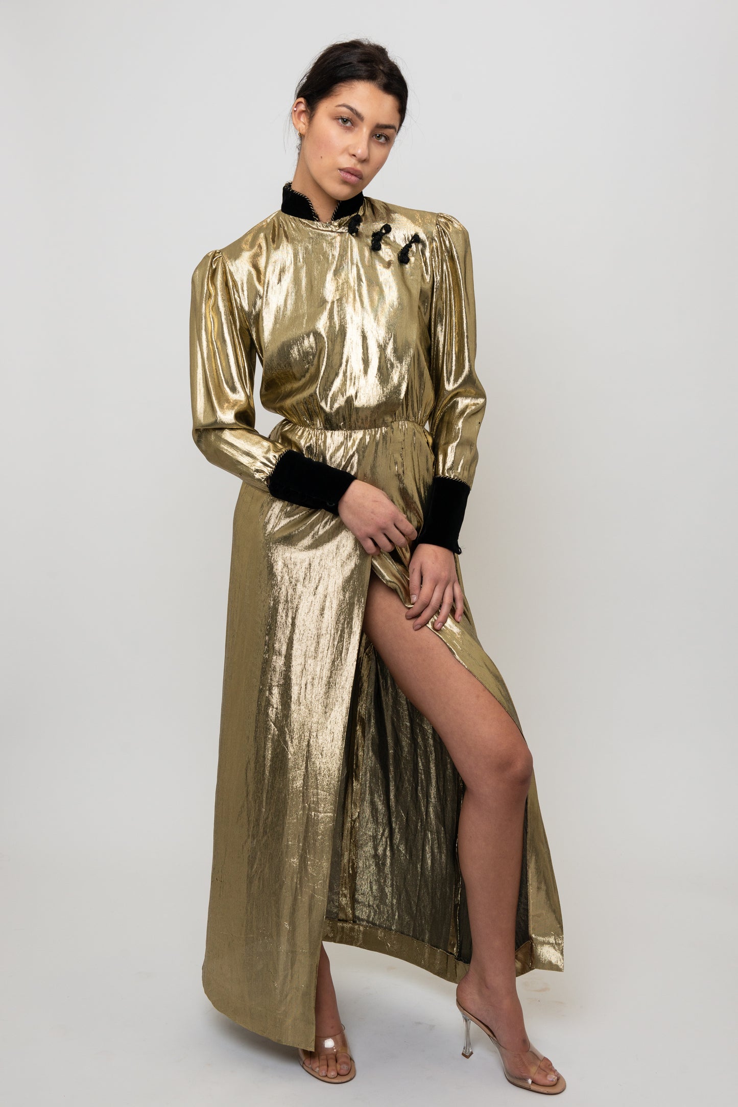 Woman wearing a gold metallic dress with a high slit on a white background
