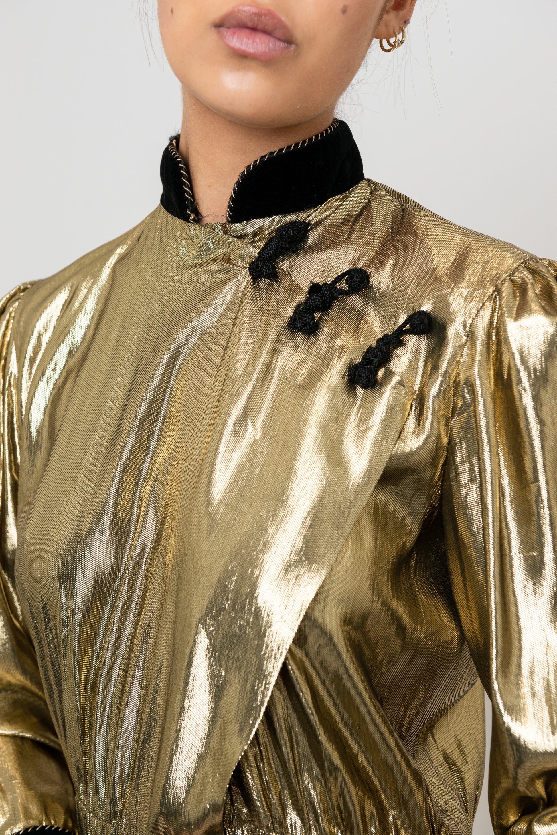 Gold metallic top with black accents worn by a person on a plain background