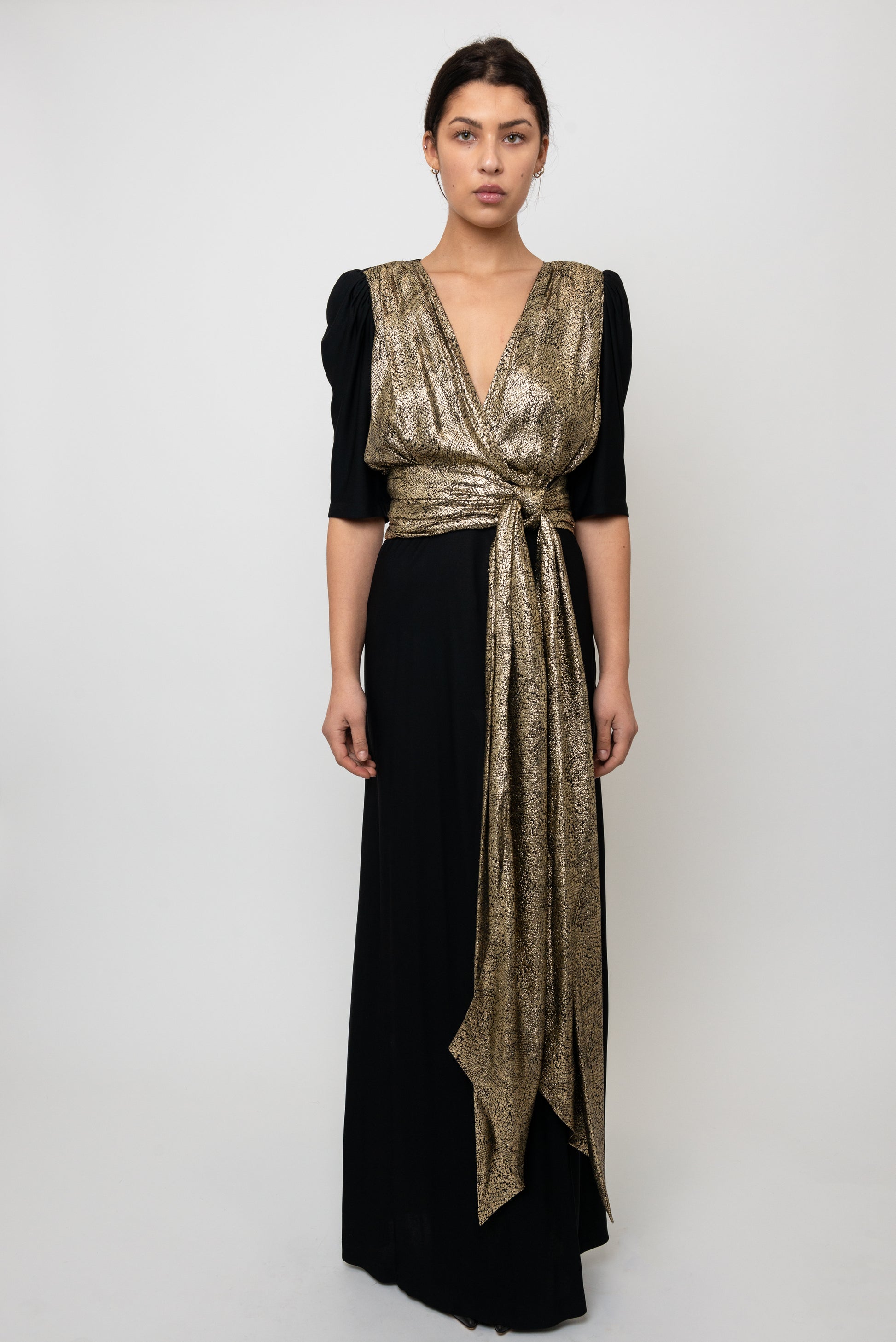 Woman wearing a black and gold dress with a plain background