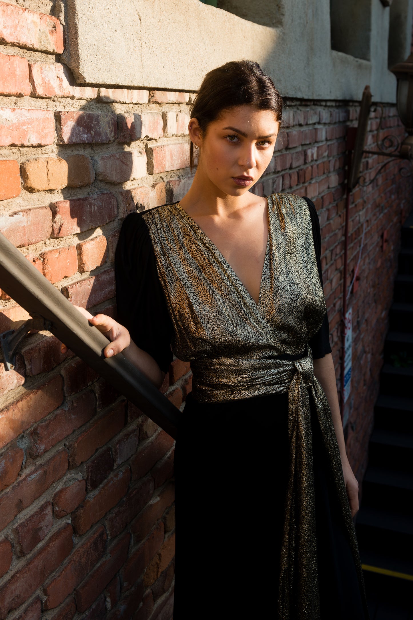 Woman in a dark dress standing against a brick wall