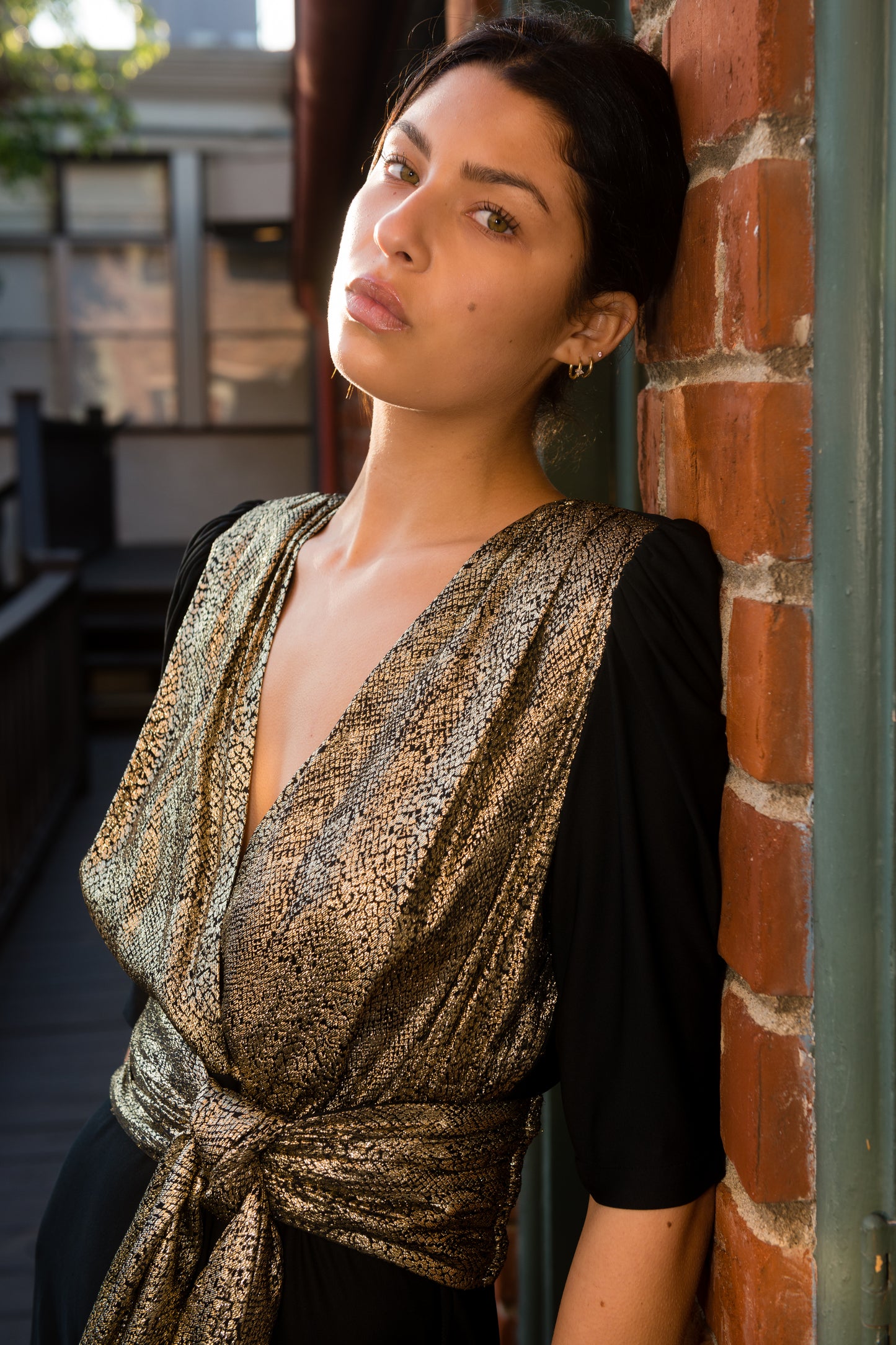 Woman leaning against a brick wall wearing a patterned top.