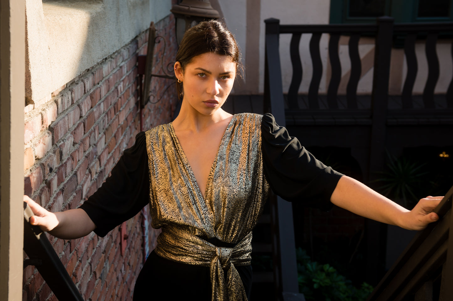 Woman in a patterned dress standing on a staircase with a brick wall background