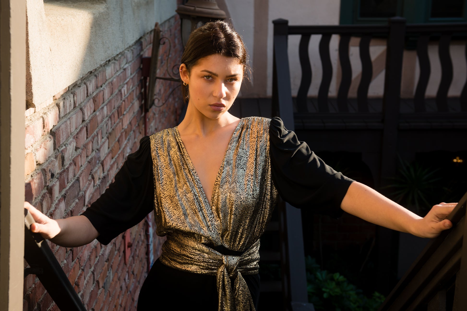 Woman in a patterned dress standing on a staircase with a brick wall background
