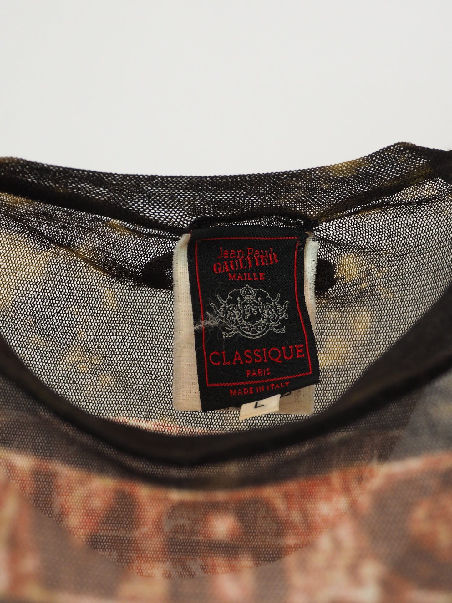 A vintage jean Paul gaultier short-sleeve t-shirt with a distressed, vintage-style graphic print featuring a tropical palm tree scene in shades of red, brown, and beige, with tribal-style patterns on the shoulders and hem.