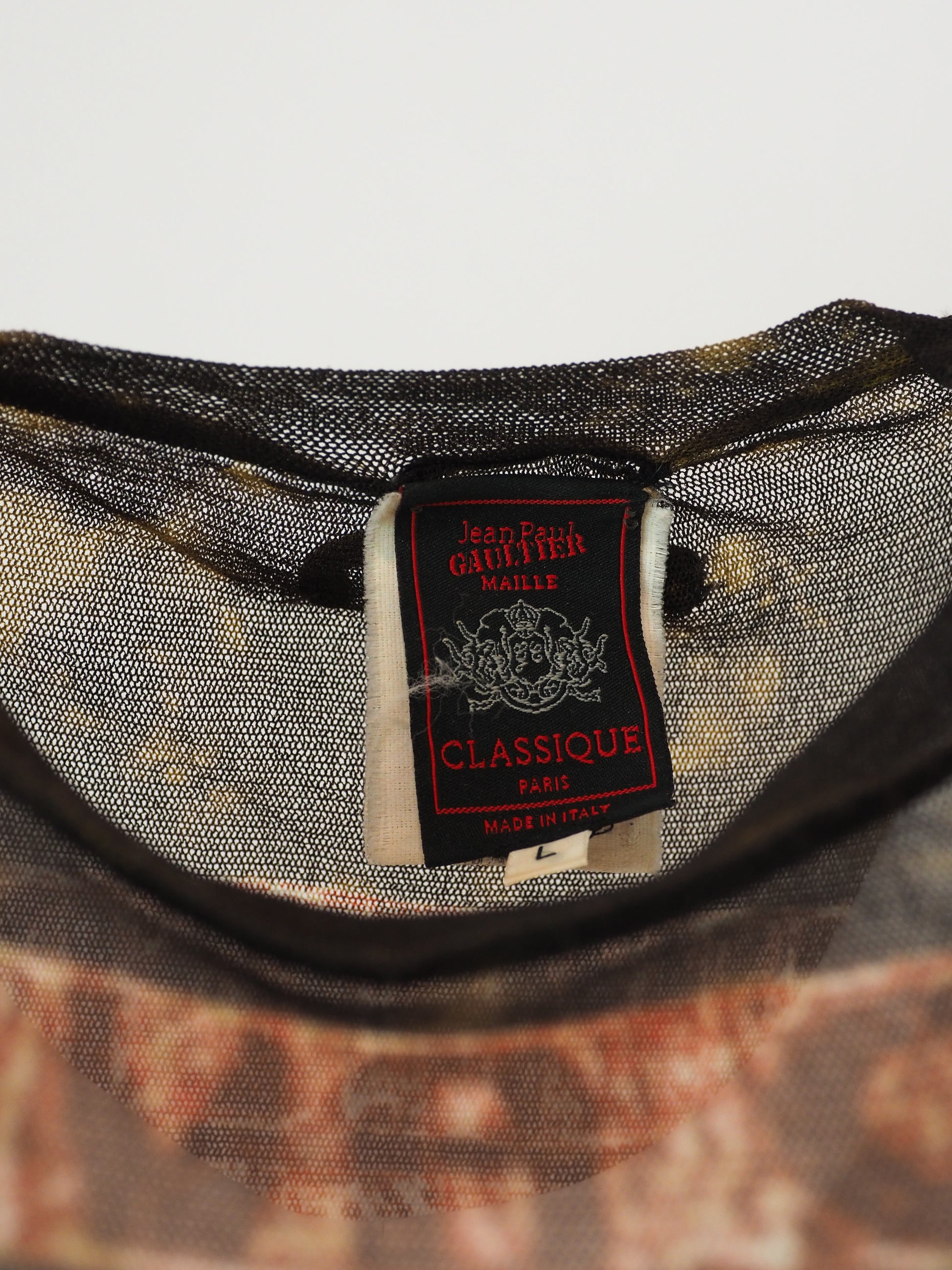 A vintage jean Paul gaultier short-sleeve t-shirt with a distressed, vintage-style graphic print featuring a tropical palm tree scene in shades of red, brown, and beige, with tribal-style patterns on the shoulders and hem.