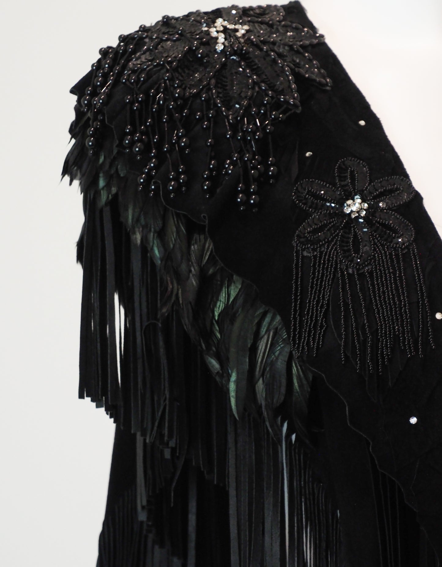 Black garment shoulder with floral embellishments and fringe details on a white background