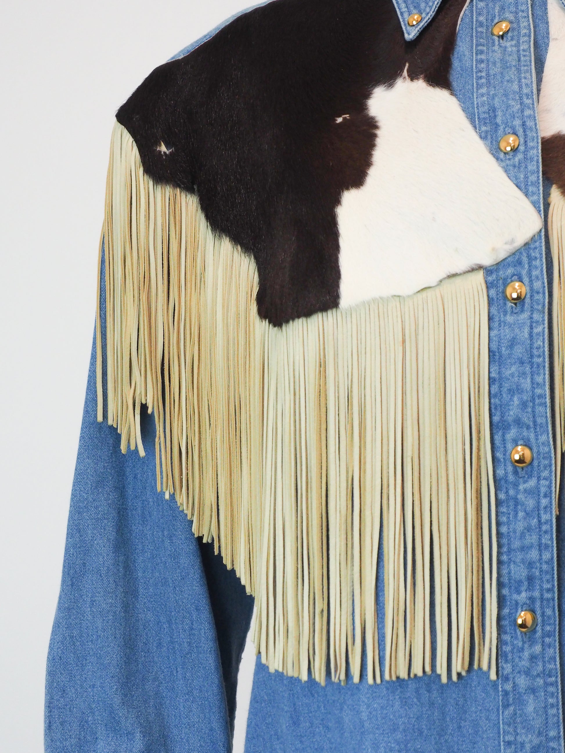 Denim shirt with cowhide leather and fringes on a plain background