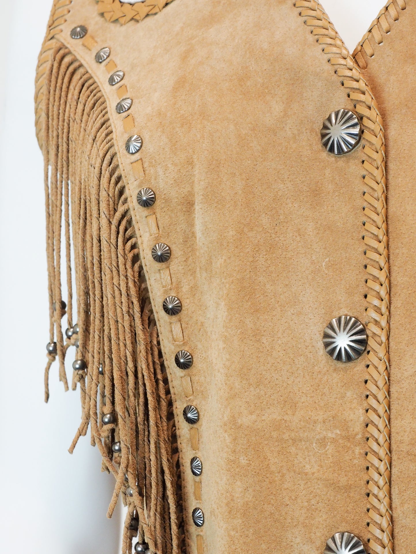 Close-up of a tan leather vest with fringe and silver studs on a white background