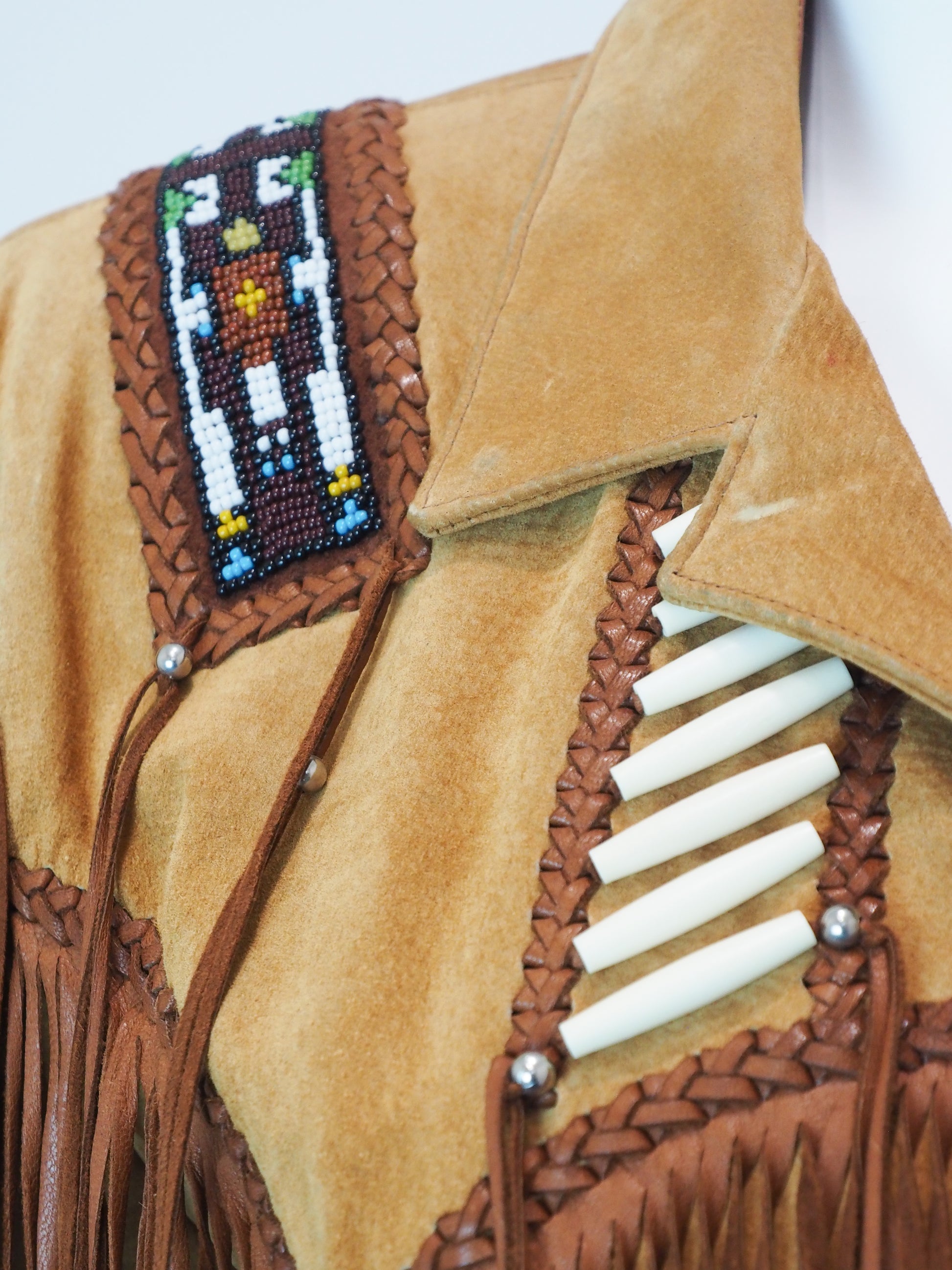 Close-up of a tan leather jacket with intricate beadwork and white fringe details.