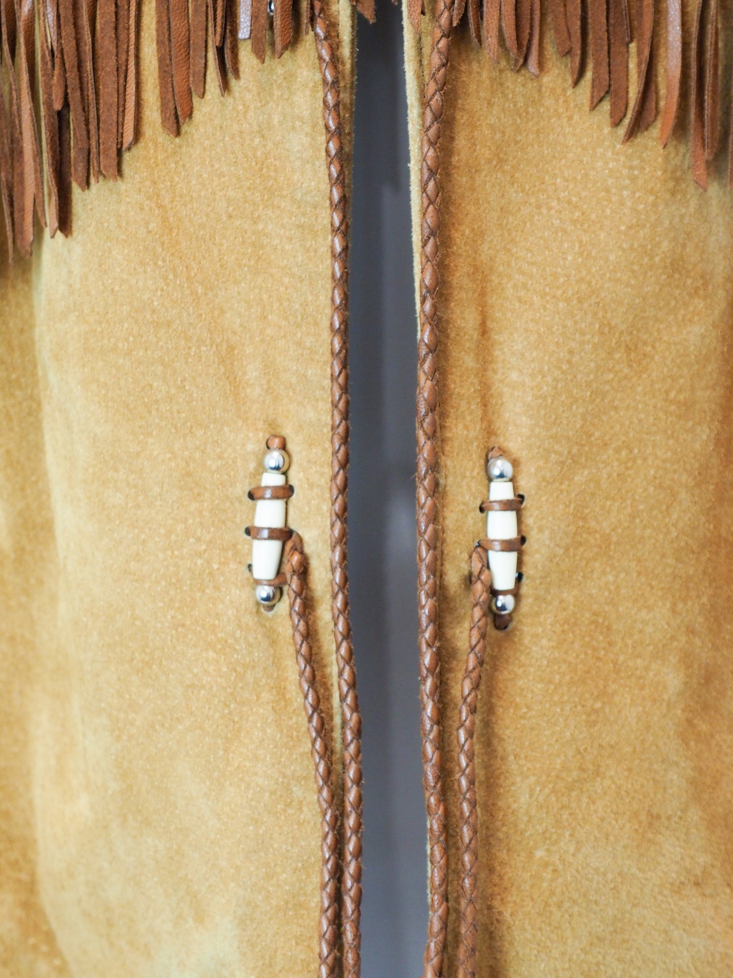 Close-up of a tan leather jacket tassel with brown fringe and braided details.