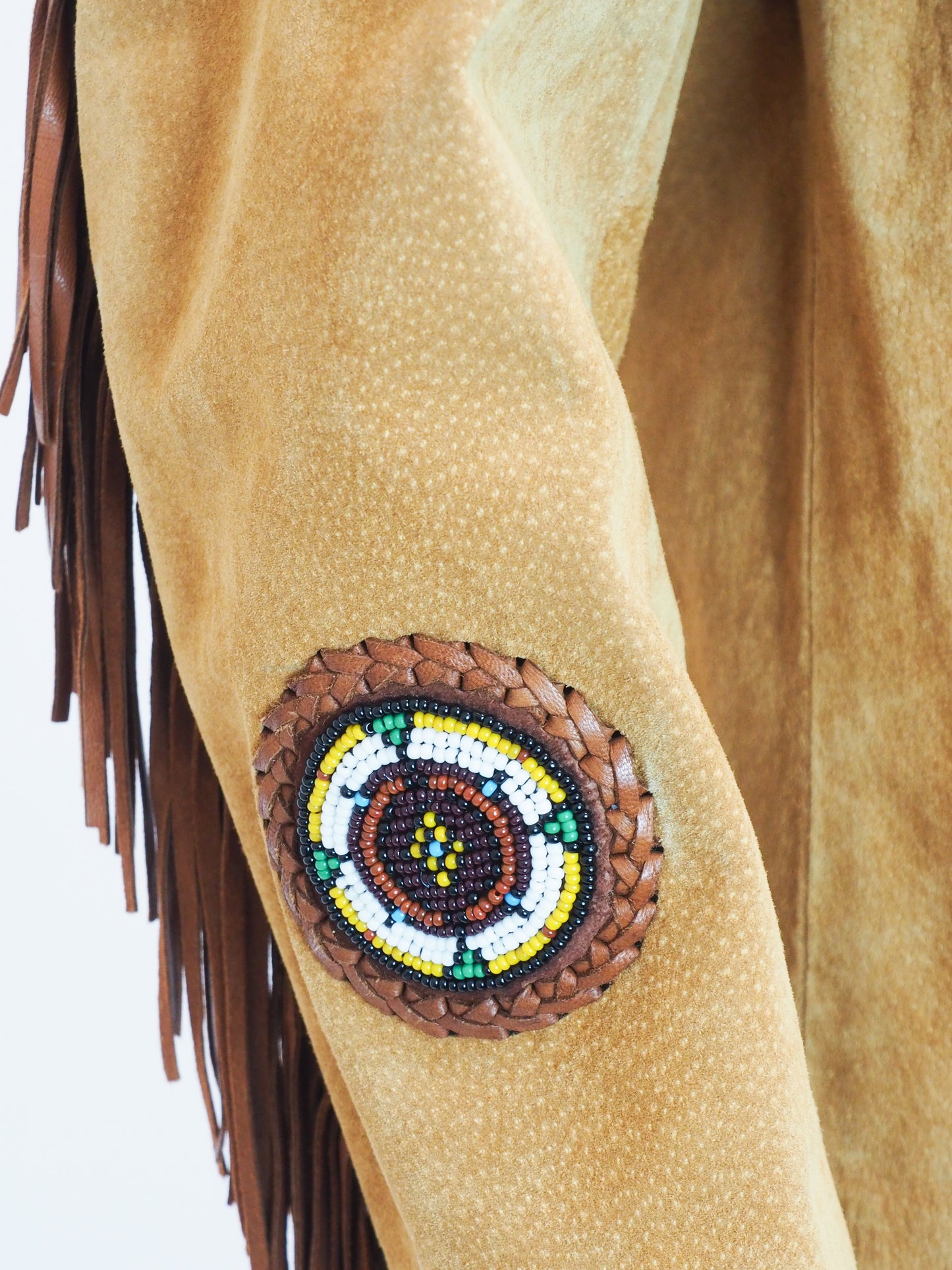 Close-up of a tan leather sleeve with a beaded design and fringes on a white background