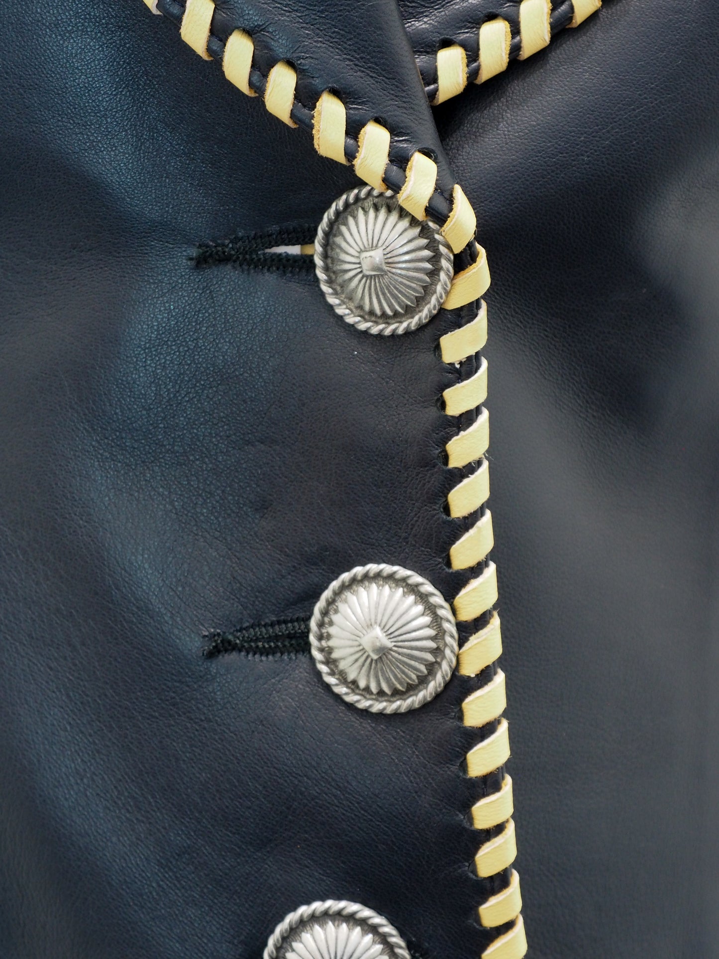 Close-up of a black leather jacket with gold zipper and silver concho details.