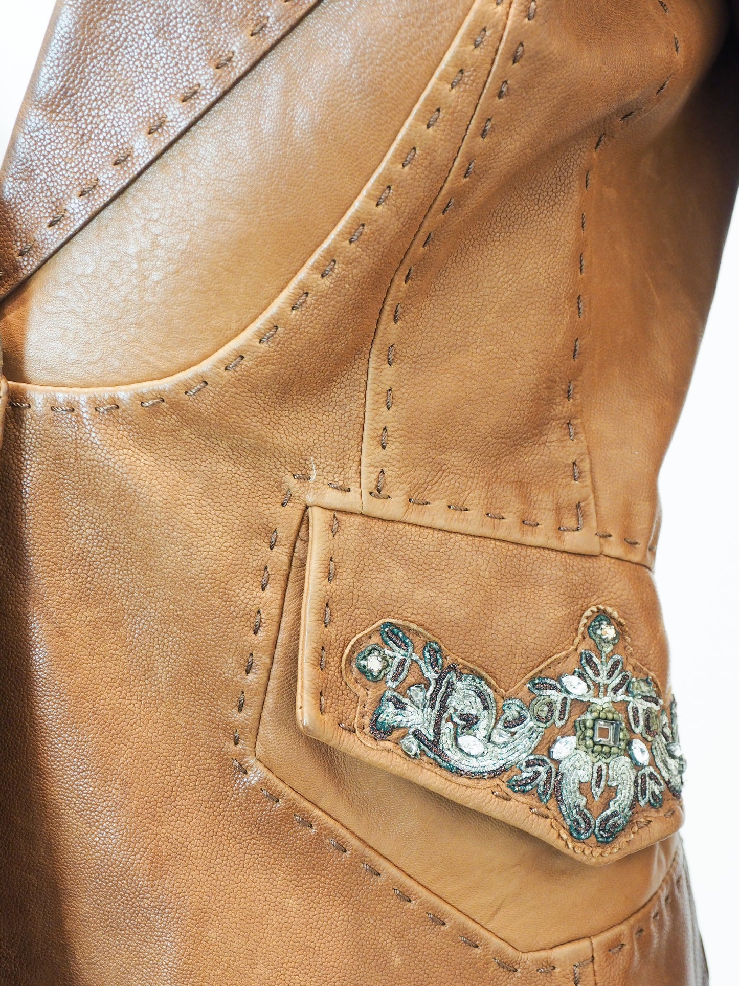 Close-up of a tan leather jacket with decorative stitching and embellishments.