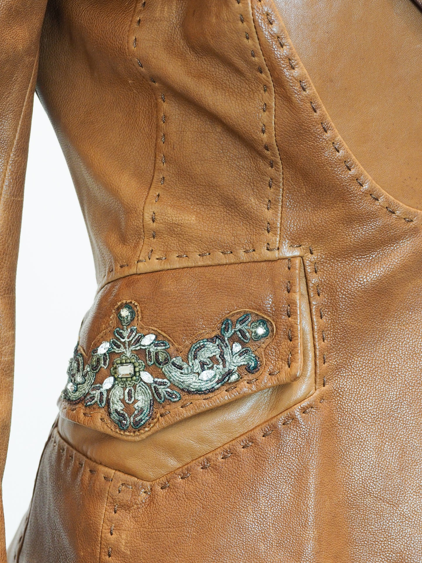 Close-up of a brown leather jacket with decorative metal emblem.