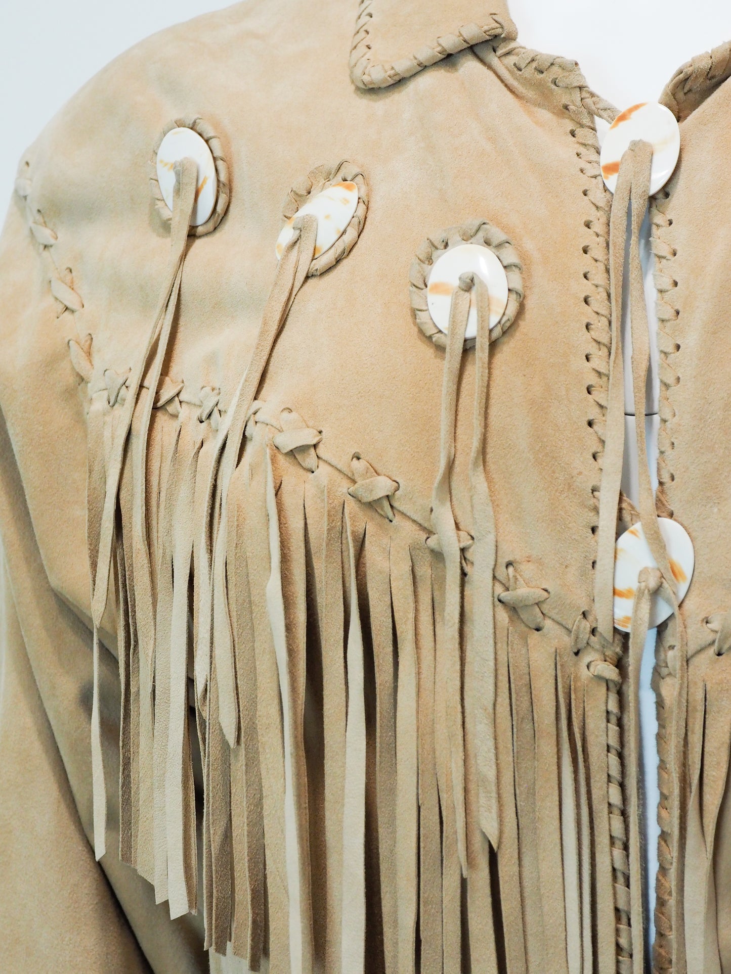 Close-up of a beige leather jacket with fringes and decorative elements on a white background