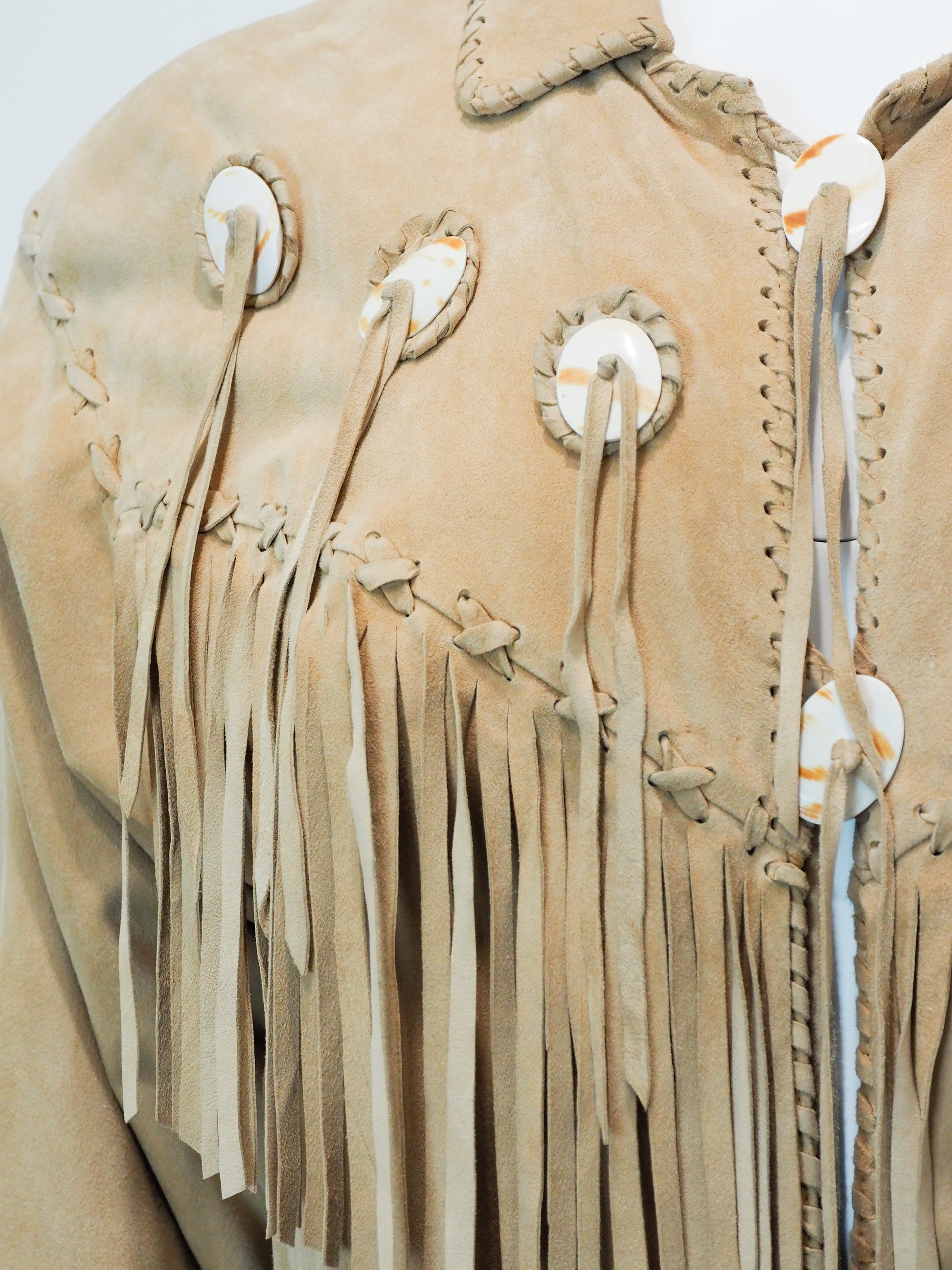 Close-up of a beige leather jacket with fringes and decorative elements on a white background
