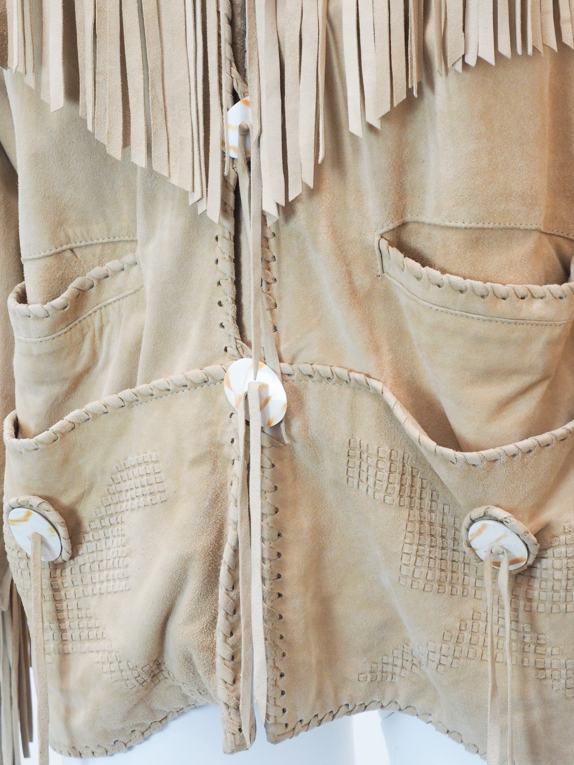 Close-up of a beige jacket with fringes and button details on a white background