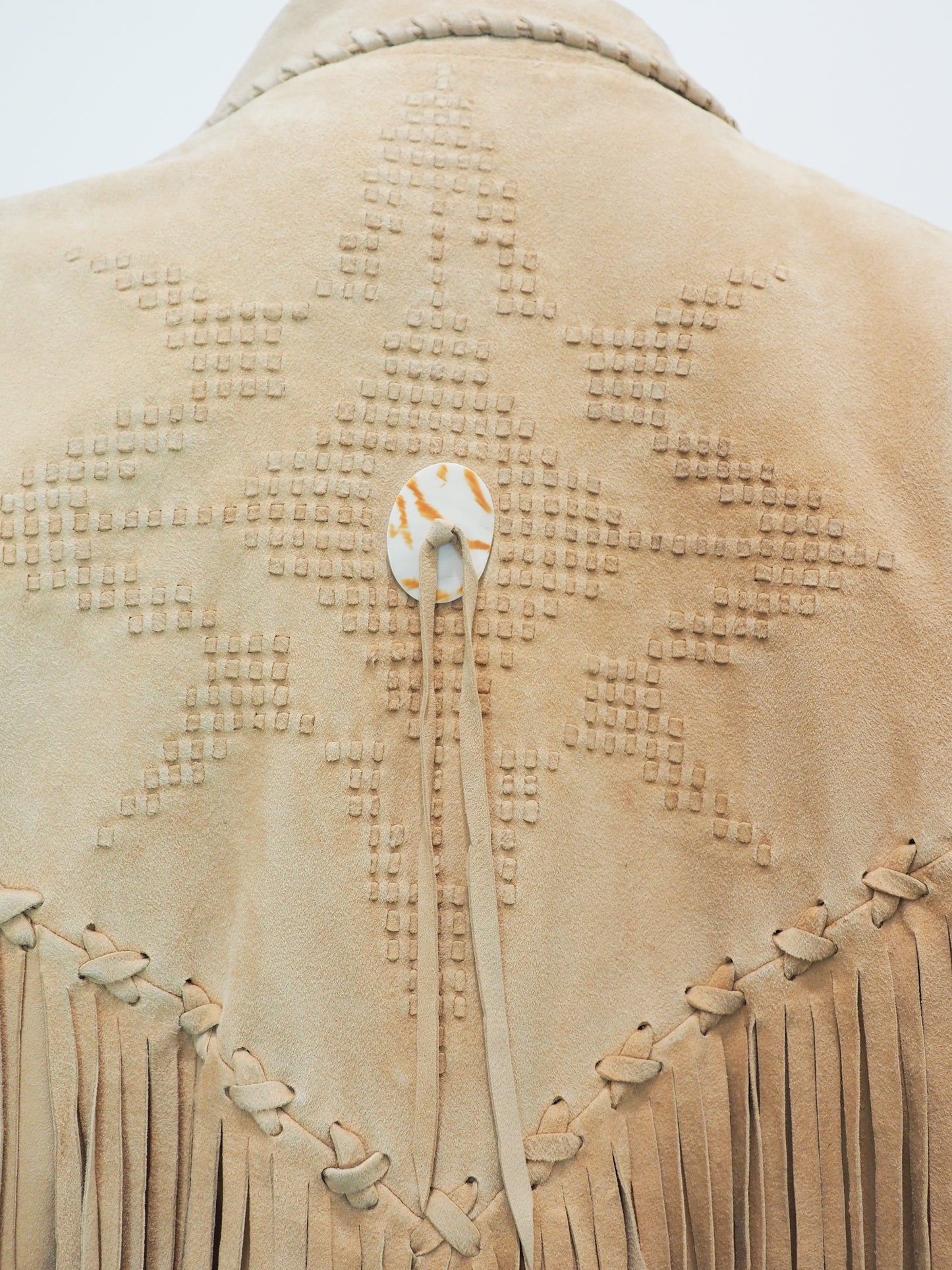 Close-up of a beige leather jacket with intricate patterns and fringes on a light gray background