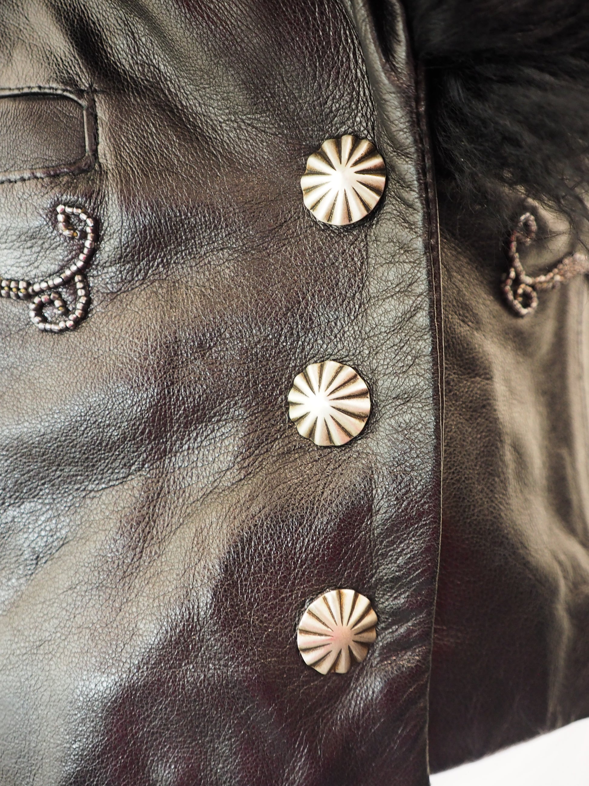 Close-up of a dark leather jacket with gold decorative buttons and patterns.